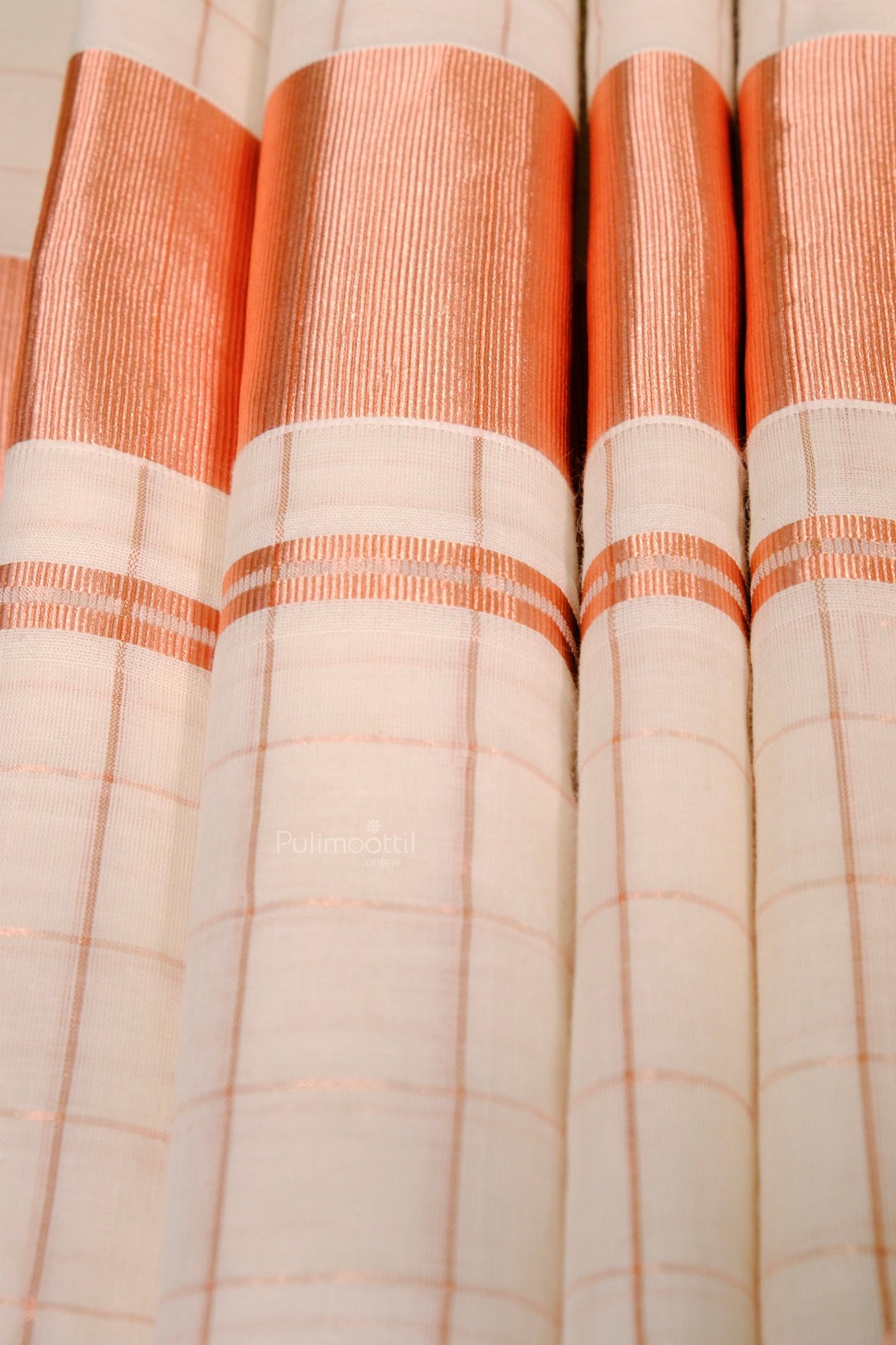 Close-up of traditional off-white Kerala Kasavu saree featuring a rich copper zari pallu and checkered weave pattern.