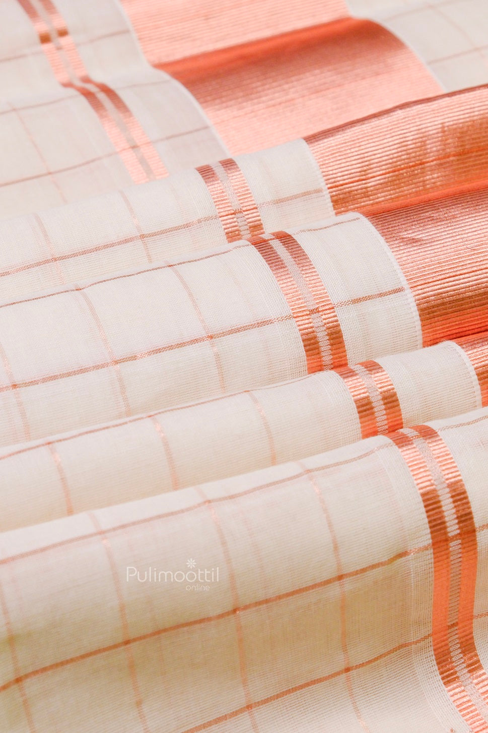 Flowing Kerala Kasavu saree with copper checks and lustrous zari detailing, spread out to show texture and craftsmanship.