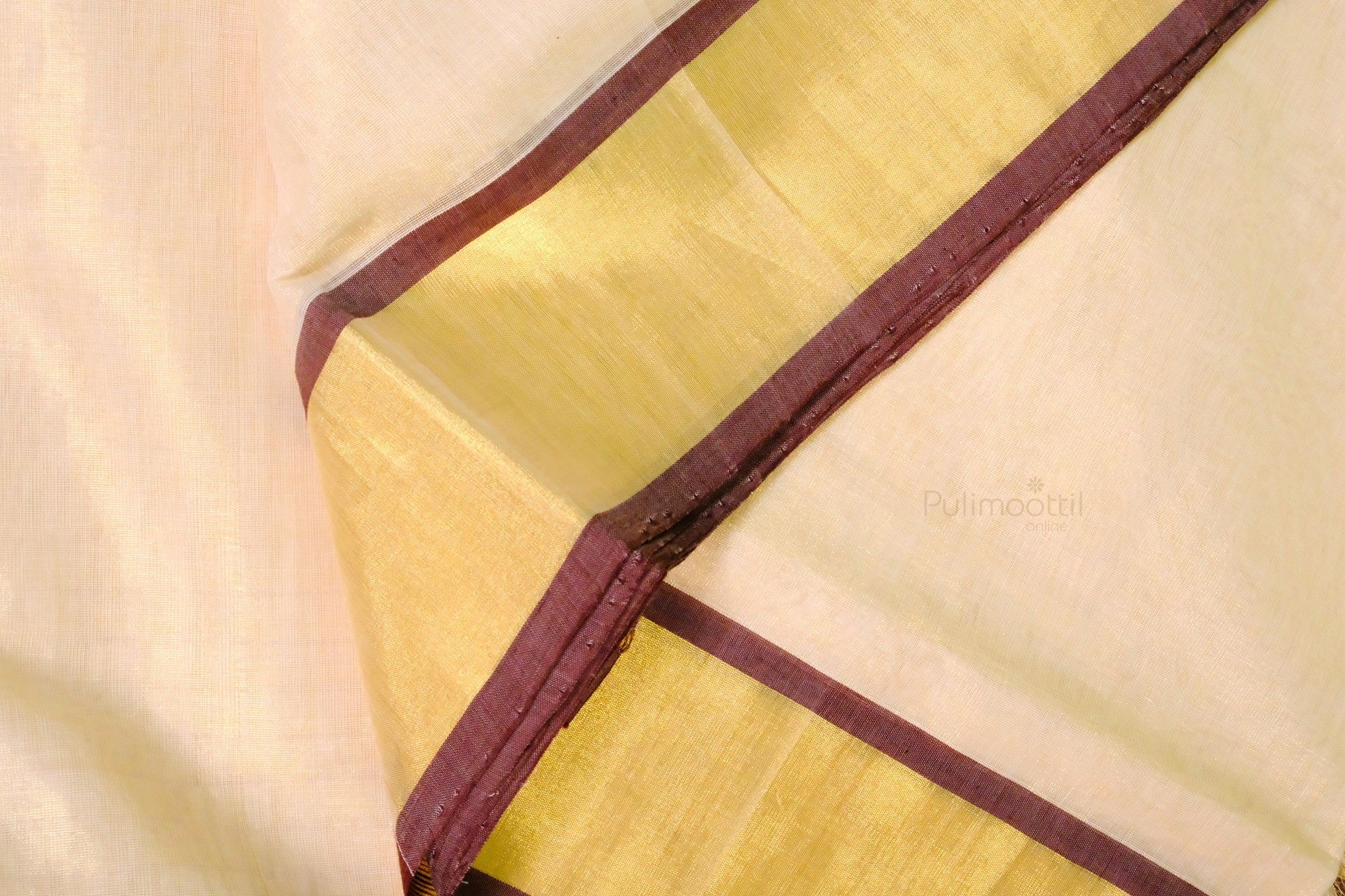 Folded Kerala saree with an off-white body and shimmering golden border edged with maroon piping.