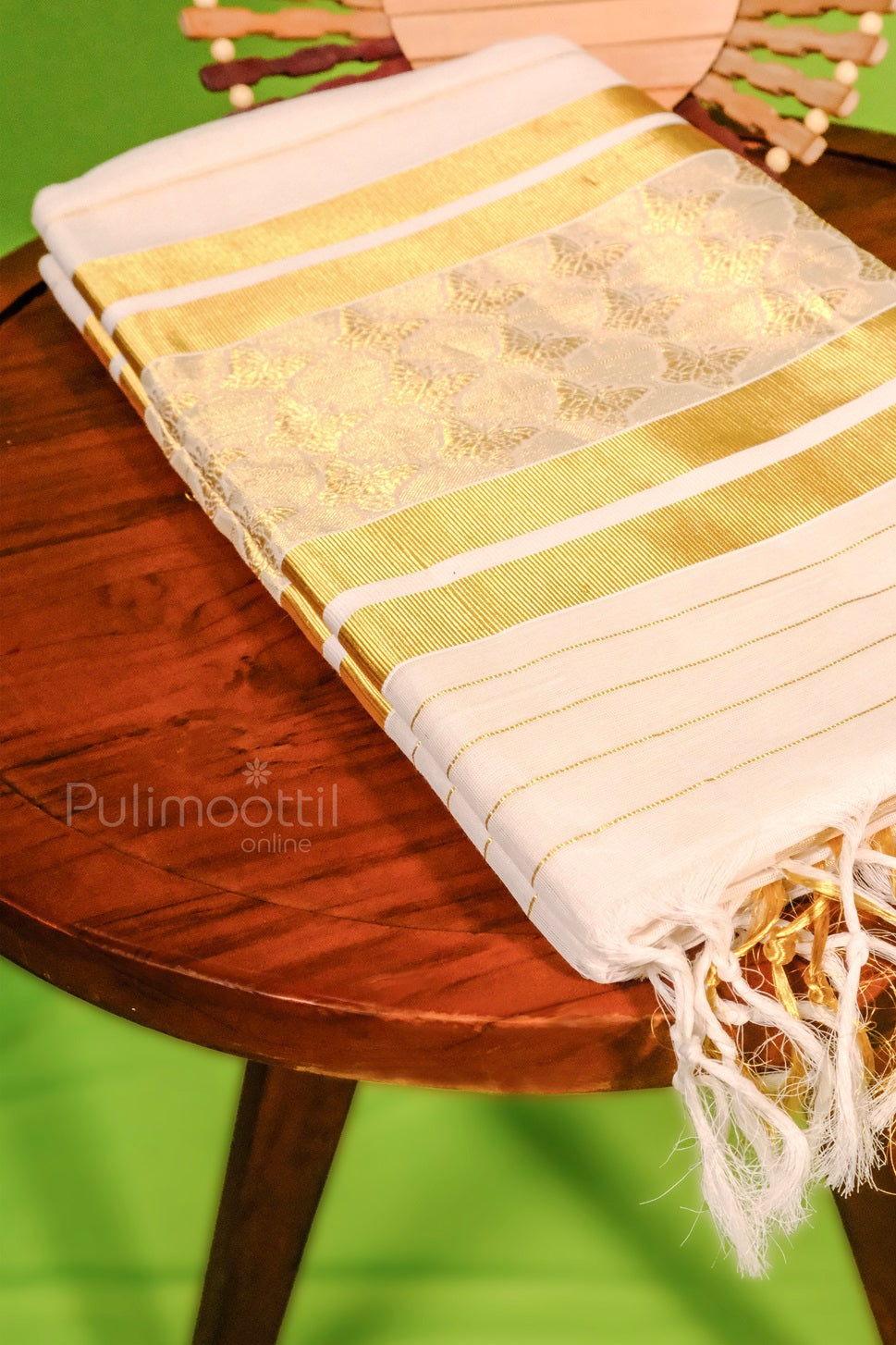 Traditional Kerala kasavu saree neatly folded on a wooden surface, featuring a rich golden zari border and subtle butterfly motifs.