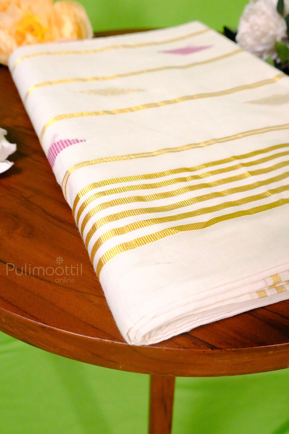 Folded Kerala kasavu saree with golden zari border and pink geometric motifs placed on a wooden table