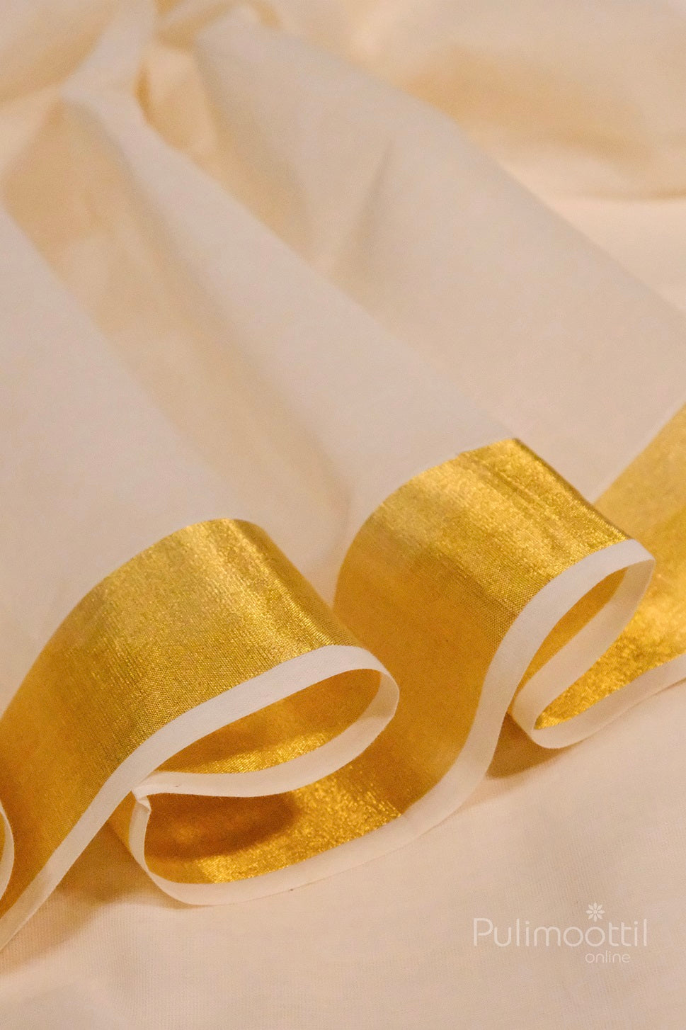 Folded section of a Kerala kasavu saree highlighting the shimmering golden zari border against the soft off-white fabric.
