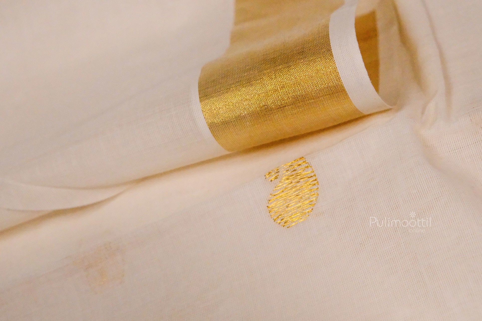 Kerala kasavu saree with a single golden paisley motif and shiny golden border, partially unfolded on a surface.