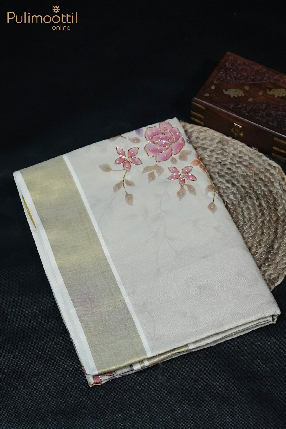 Kerala traditional tissue saree folded on round carpet with golden border and floral printed body, beads and sequence work – Onam Kerala saree styled with wooden box.