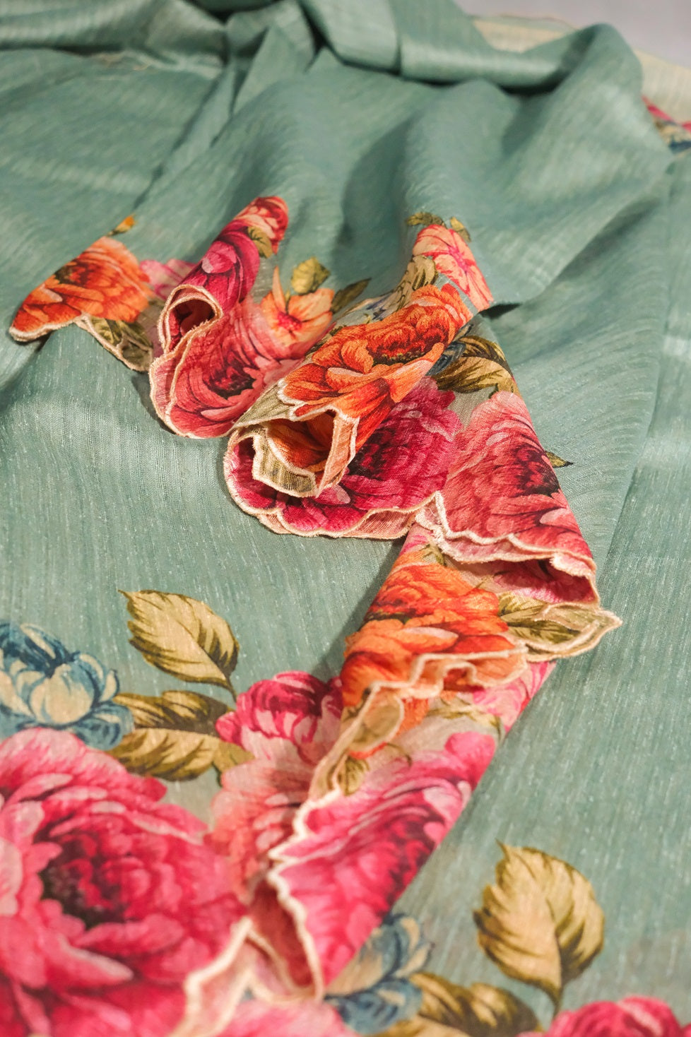 Close-up view of floral printed border on light teal semi jute saree with detailed embroidery.