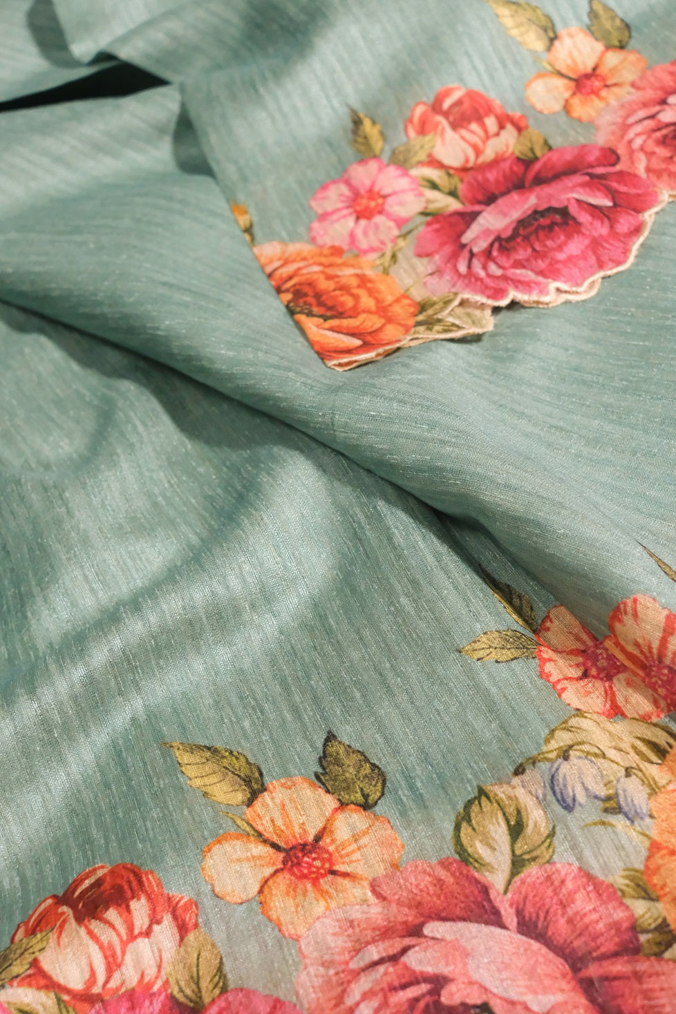 Detailed floral embroidery and design on semi jute saree in light teal color with pink and orange flower prints.