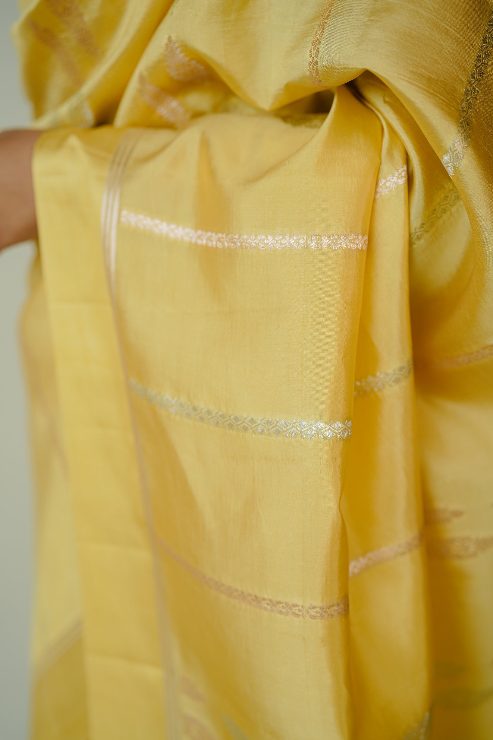 Close-up of the pallu of a yellow mango silk saree showcasing detailed silver zari weaving.