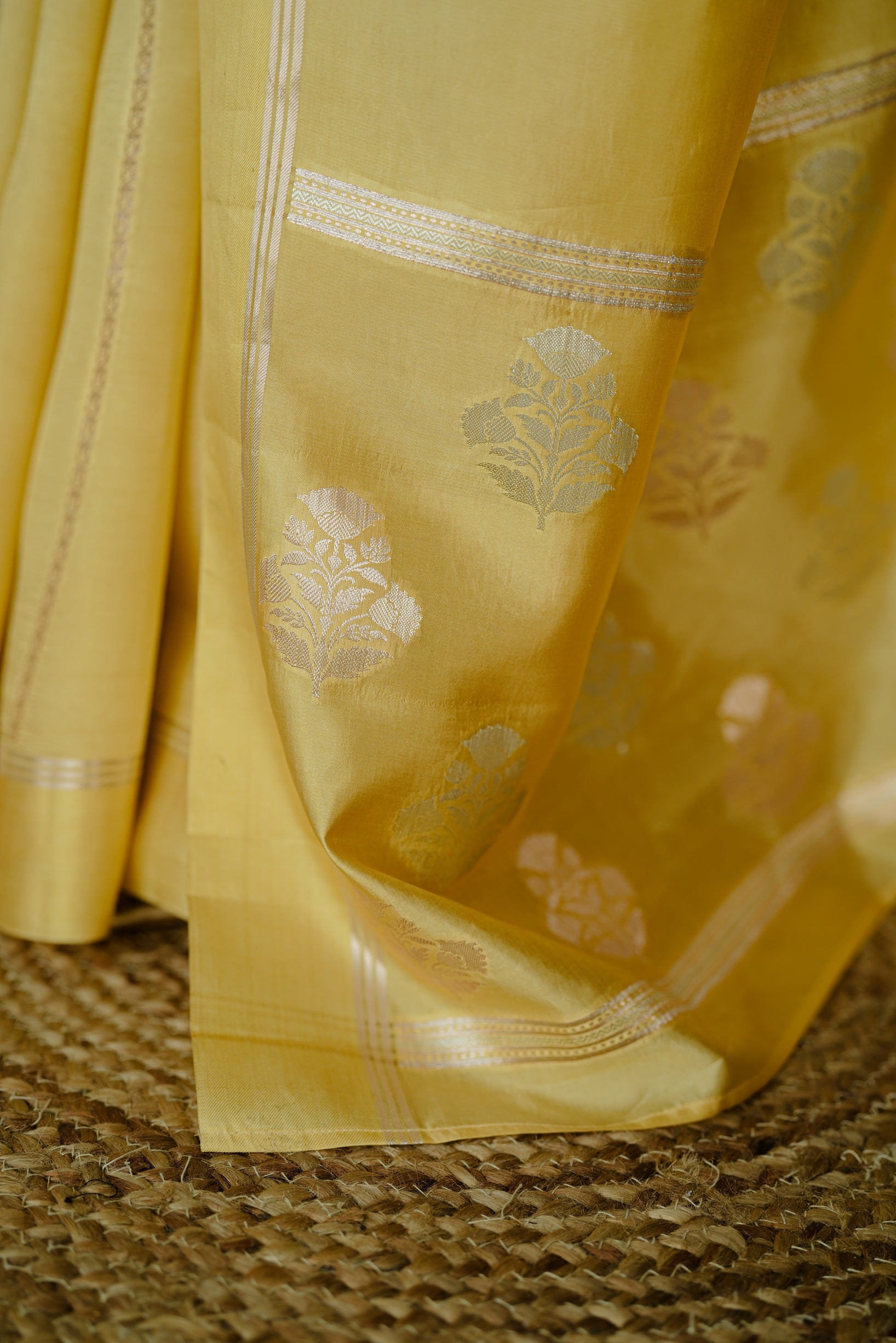 Bottom view of the saree showing traditional floral silver motifs and border work on the mango yellow silk fabric.