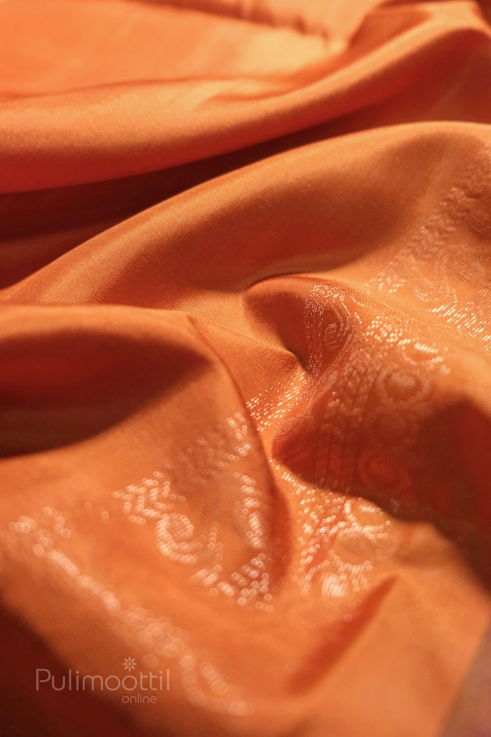 "Orange Kanchipuram soft silk saree draped with subtle gold brocade floral motifs, showing fabric folds and sheen