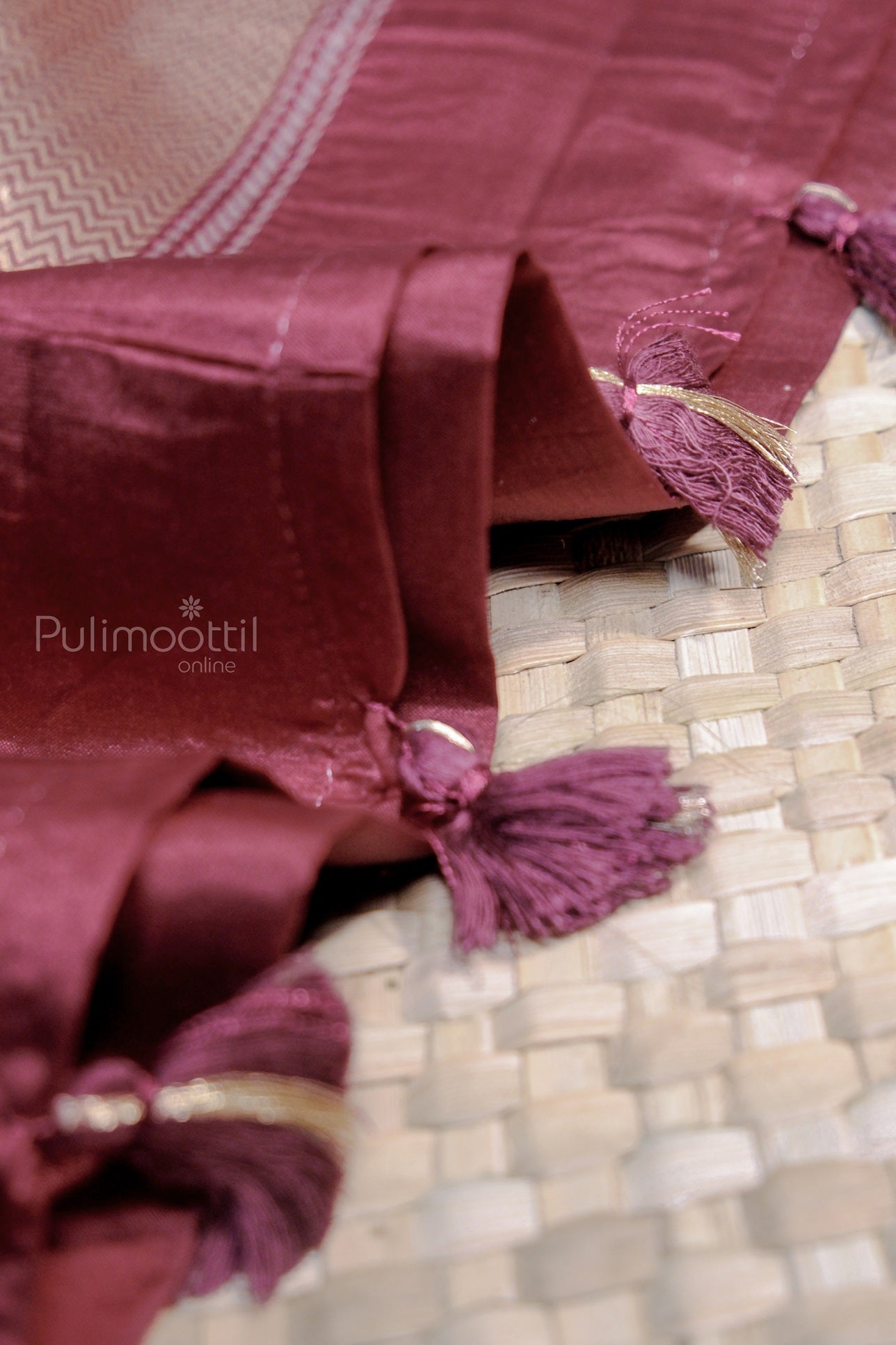 Detailed view of the cobalt blue silk saree's tasselled end with golden thread highlights on a woven mat background.