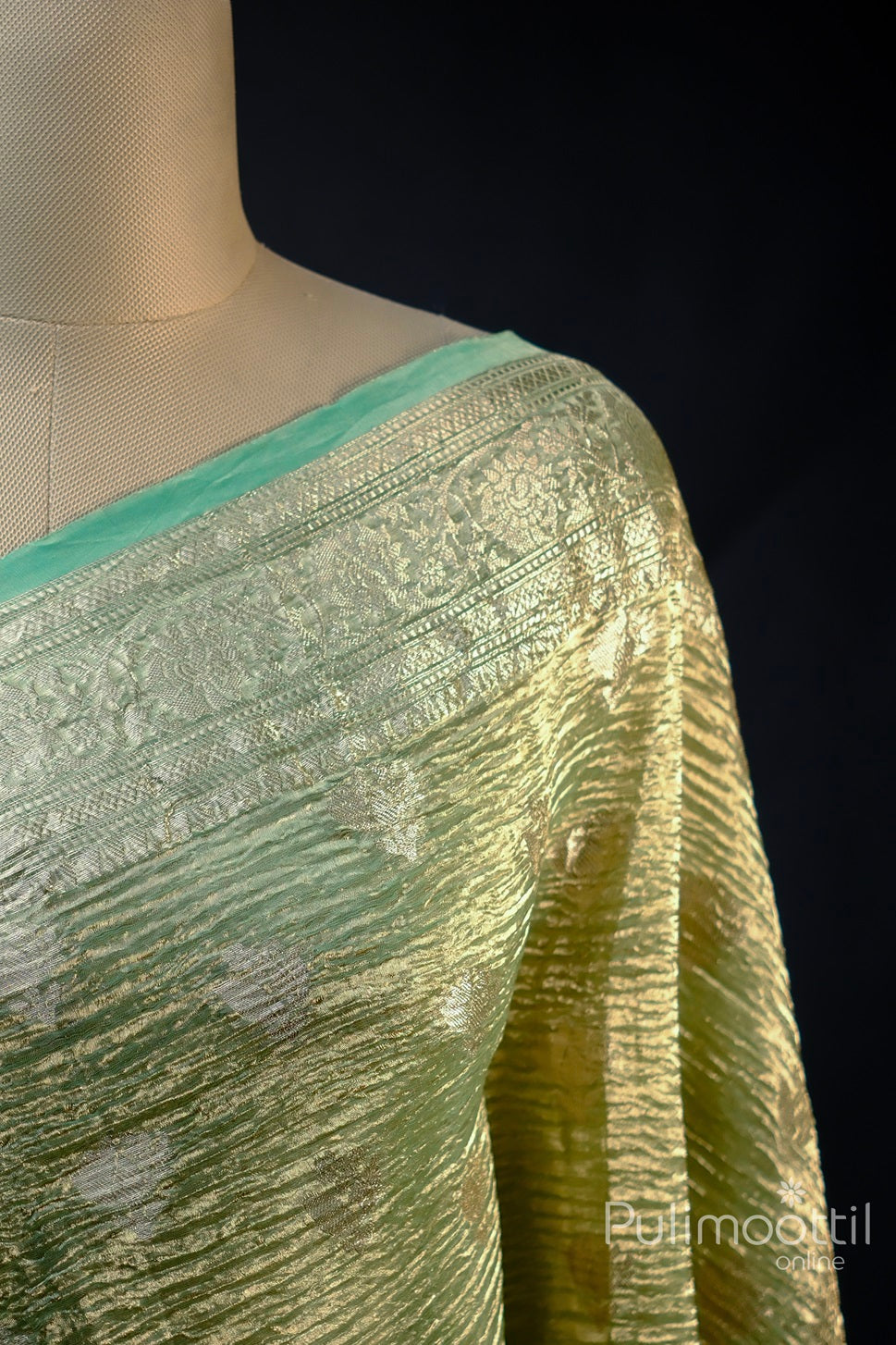 Mint green Banarasi silk saree draped over a mannequin, showcasing the delicate gold zari floral buttas and intricate floral border, with a soft green edge enhancing its elegant and luxurious look