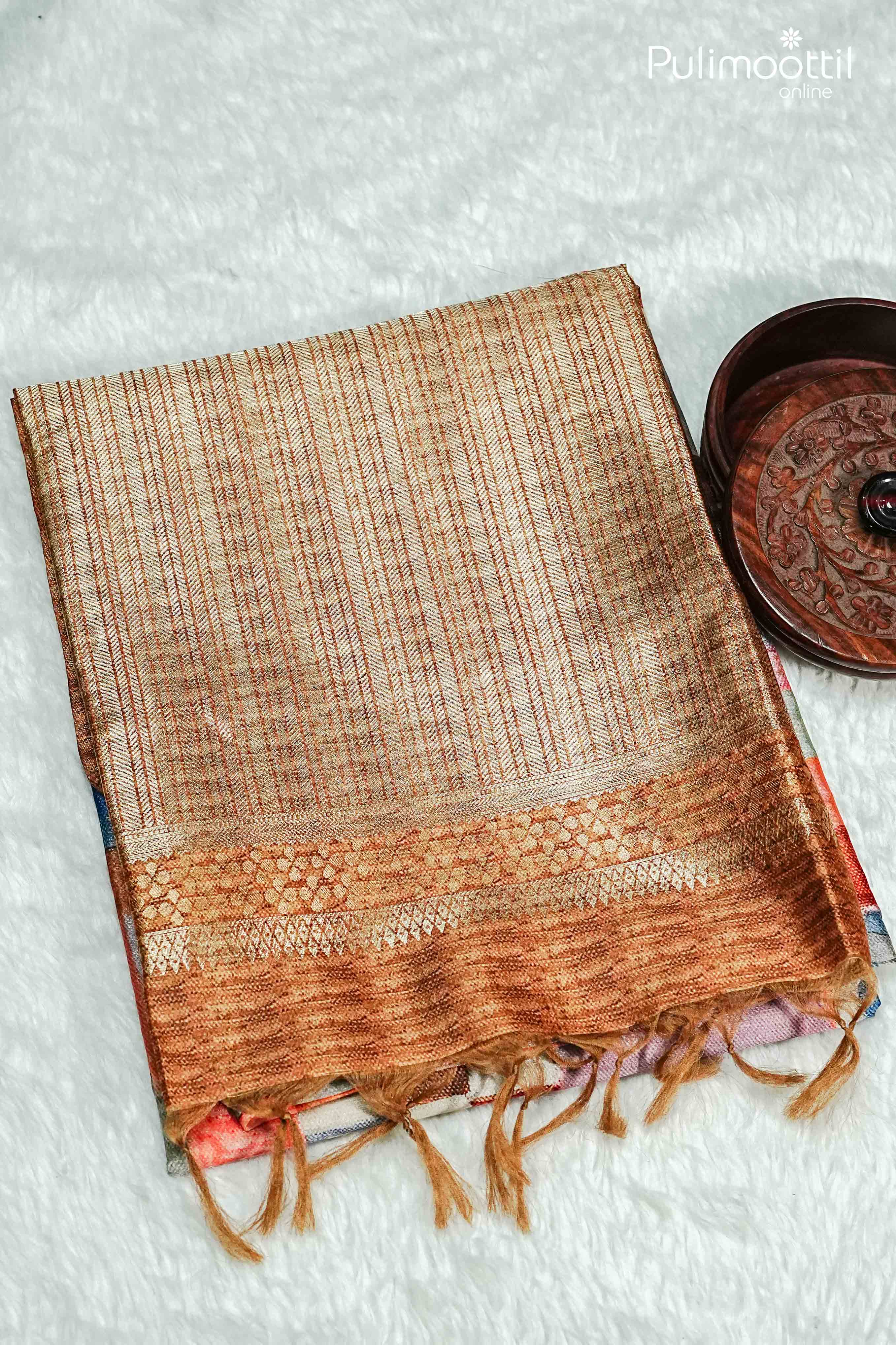 Folded multi colour semi jute saree with golden contrast pallu and woven border, placed on white textured background beside decorative wooden bowl.