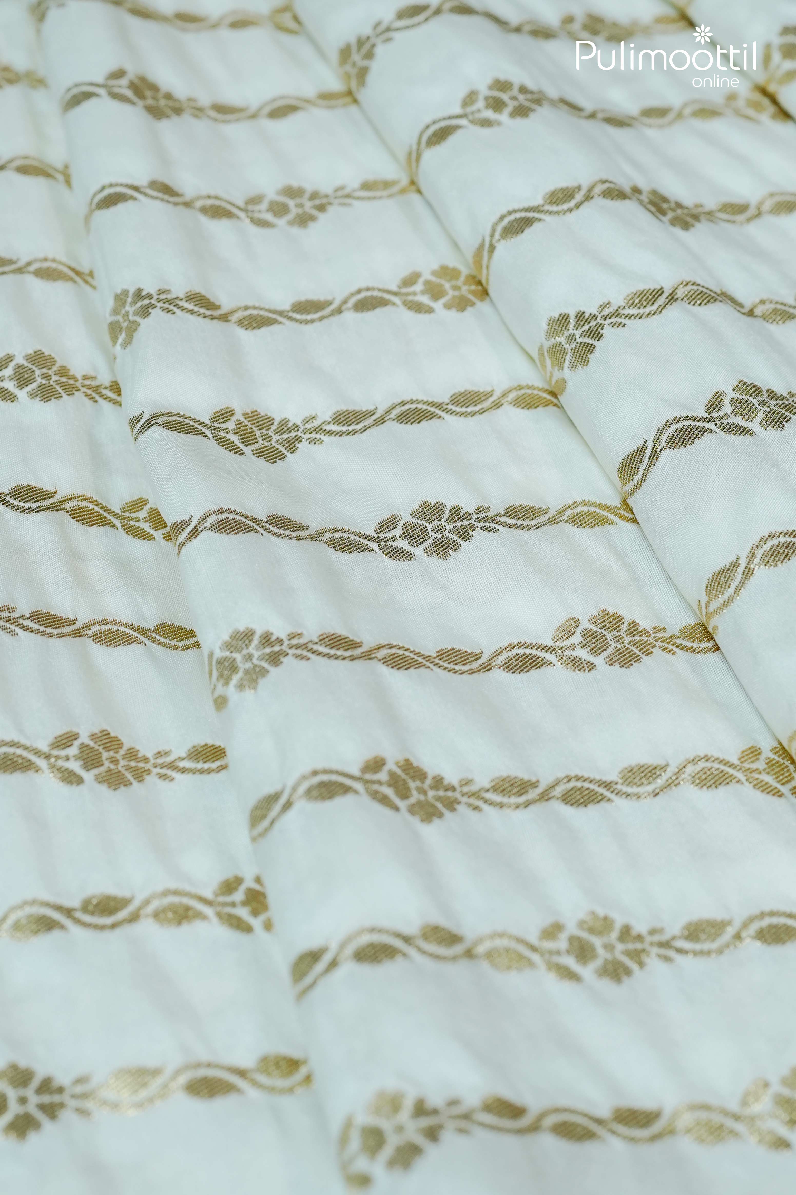 Close-up of off-white semi-silk saree fabric with intricate golden zari floral stripe design and smooth woven texture.