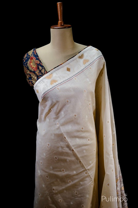 Off white Chandheri silk saree draped on mannequin, featuring elegant zari butta motifs, running stitch detailing, and designer border with contrast blouse.