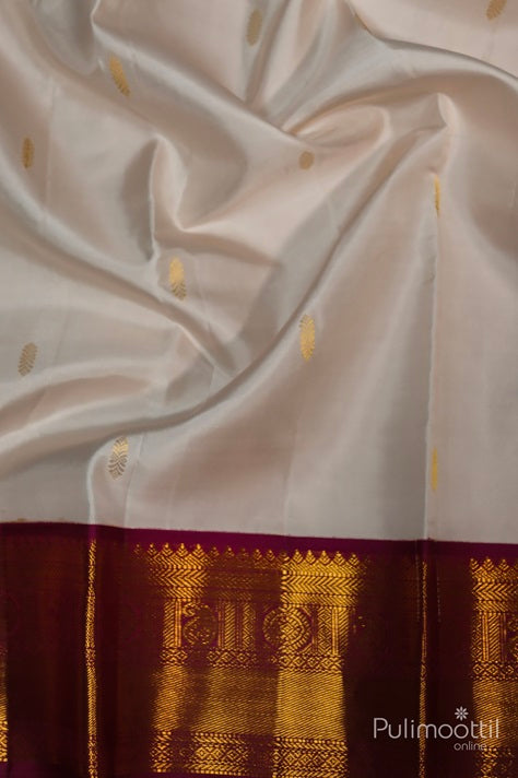 Close-up of Off White Pure Kanchipuram Silk Saree with Golden Zari Buttas and Maroon Border Featuring Intricate Traditional Design.