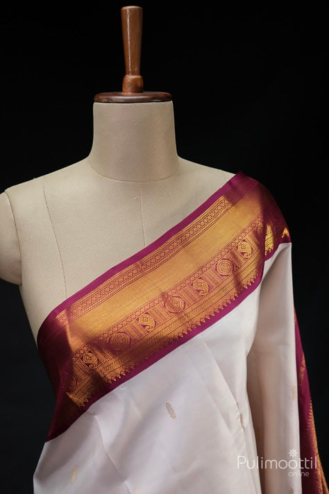 Off White Pure Kanchipuram Silk Saree with a Golden Zari Border and Maroon Contrast Border, Draped Over a Dress Form.
