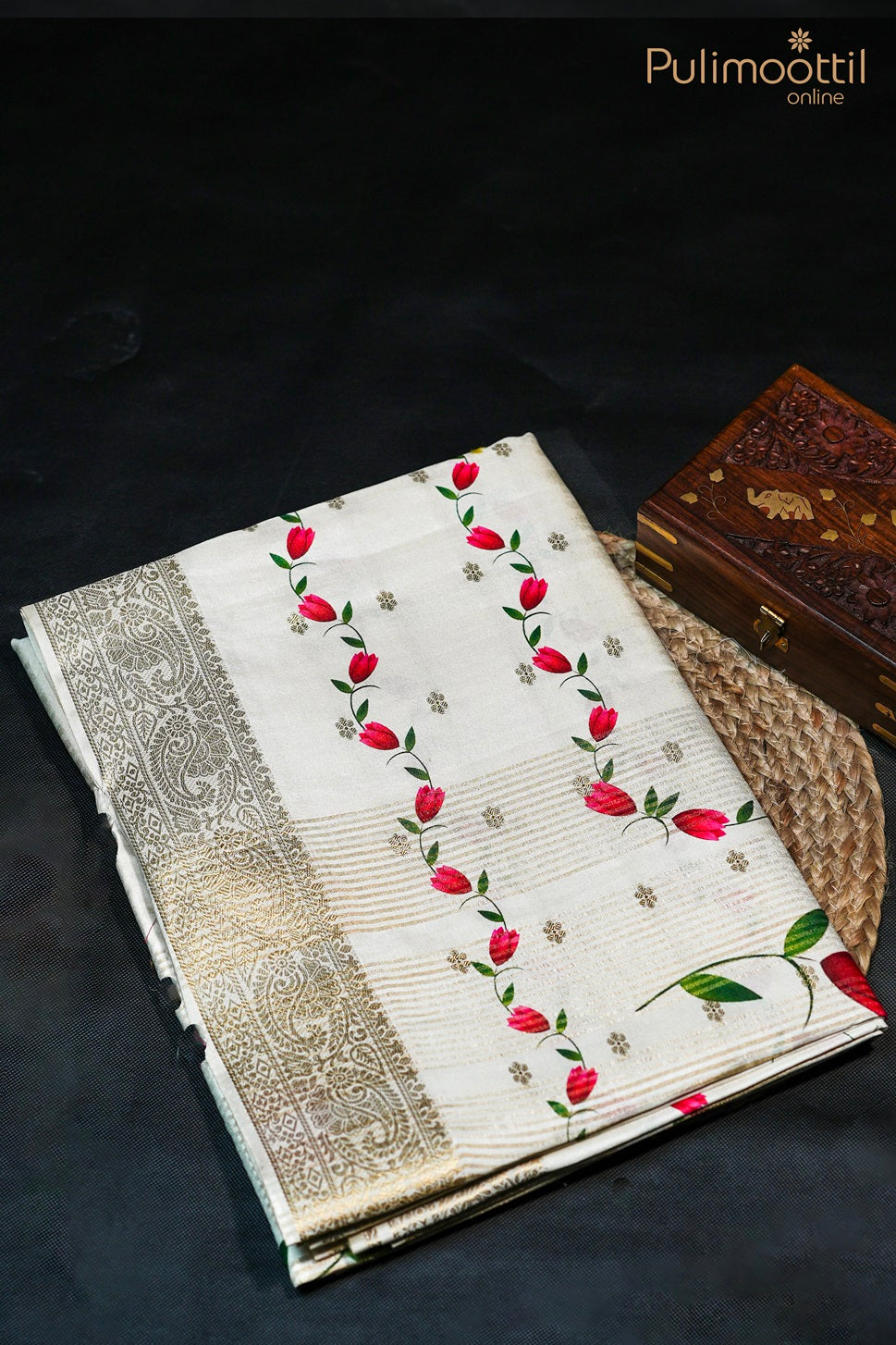 Off white semi tissue silk saree with printed body and antique zari border, displayed on mannequin placed over carpet mat with a wooden box nearby.