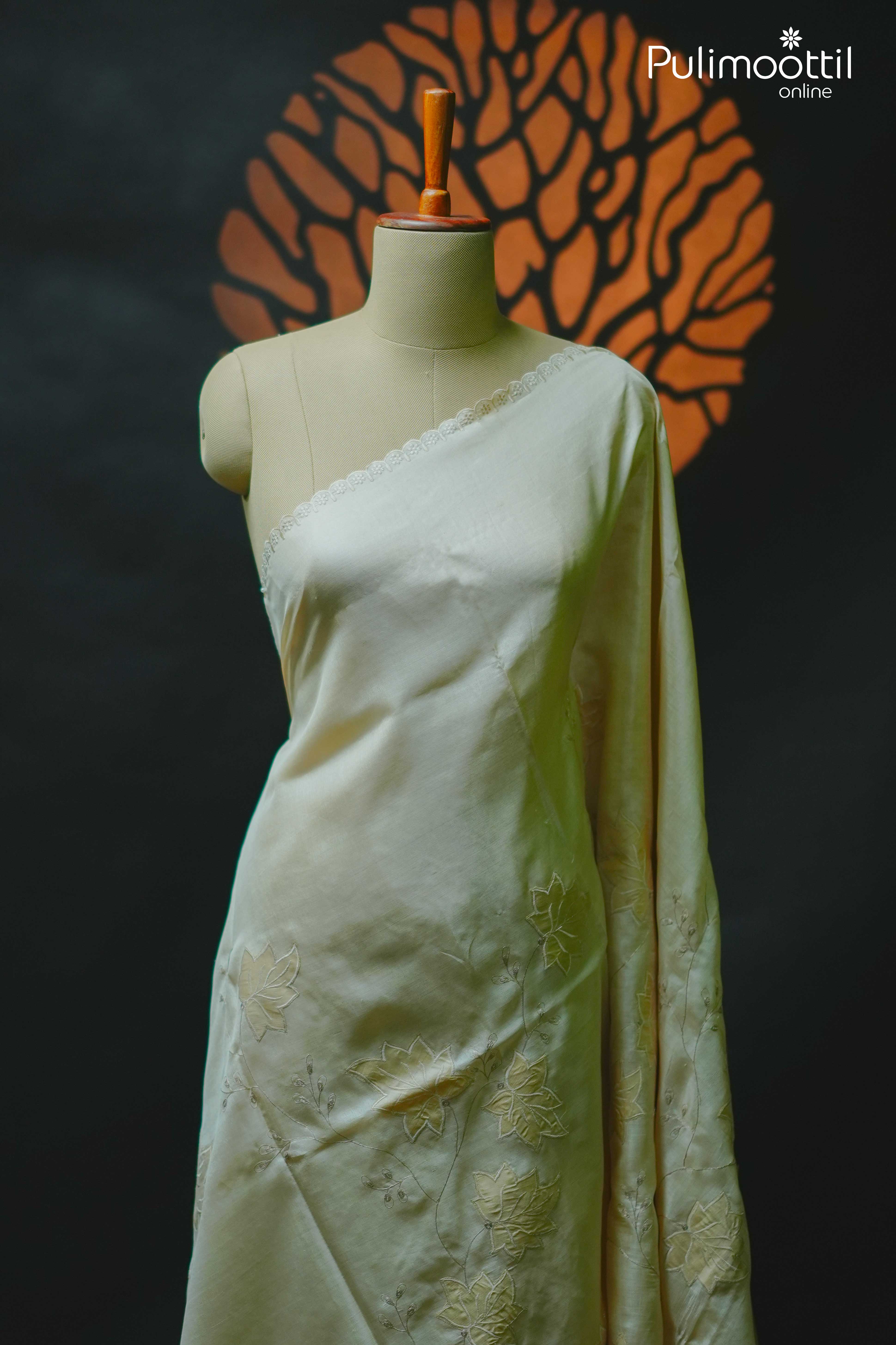 Off-white Tussar silk saree displayed on mannequin with delicate floral appliqué work and scallop lace border, perfect for festive occasions like Onam.
