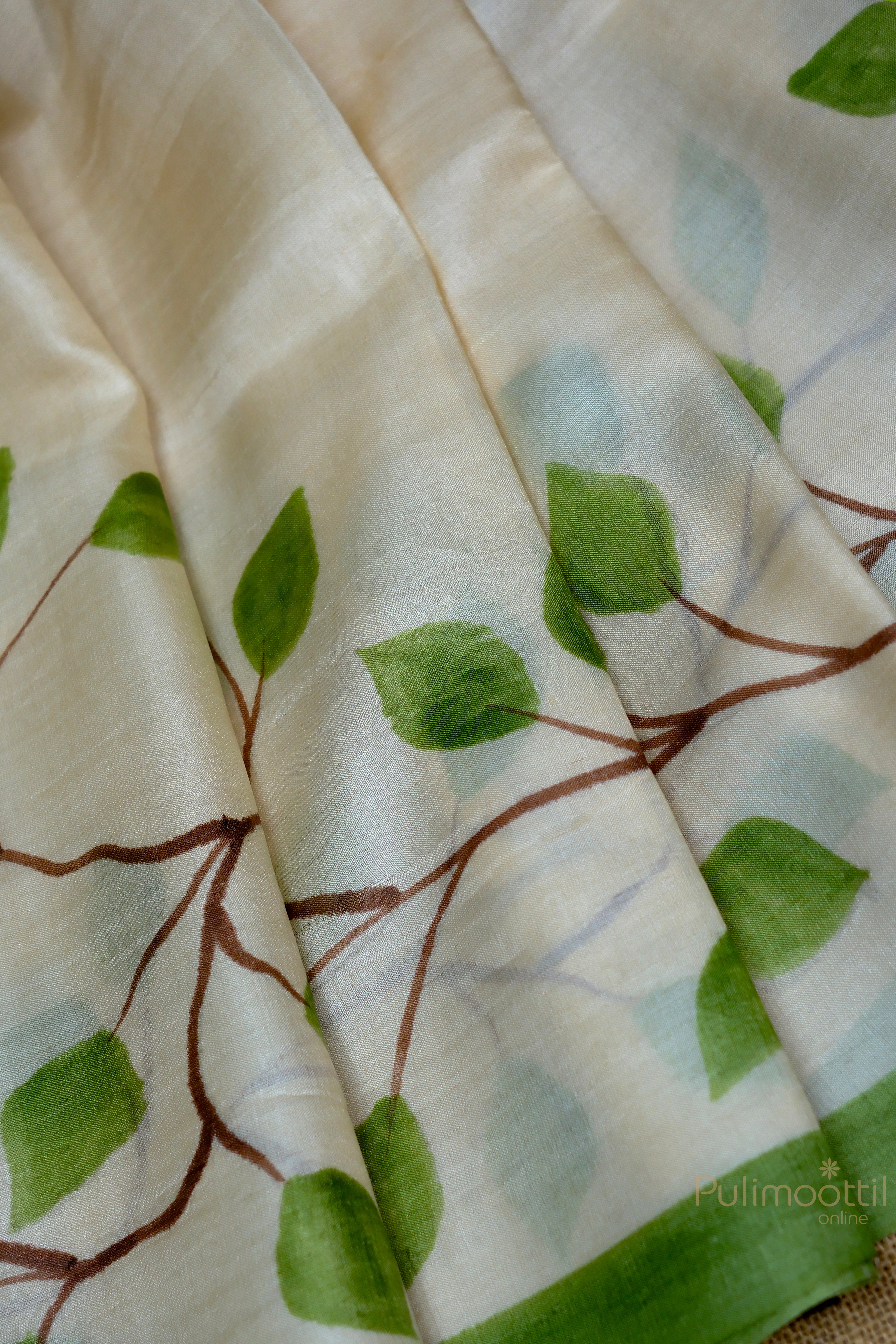 Off-white Tassar saree with floral print and a green contrast border, displayed on a mannequin from a side angle, highlighting the overall design.