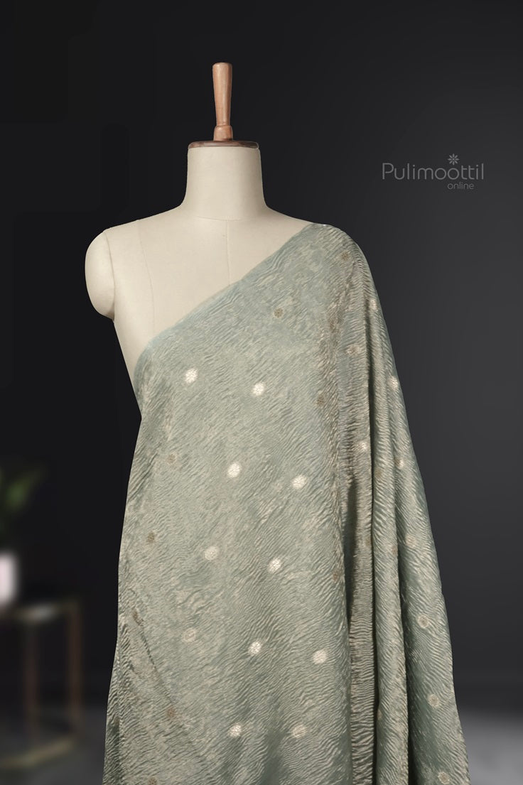 Pastel green crushed organza saree draped on mannequin, showcasing elegant golden polka embroidery.