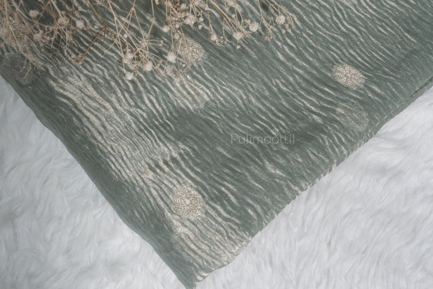 Corner shot of pastel green organza saree with zari circular motifs and dried flowers on white fur.