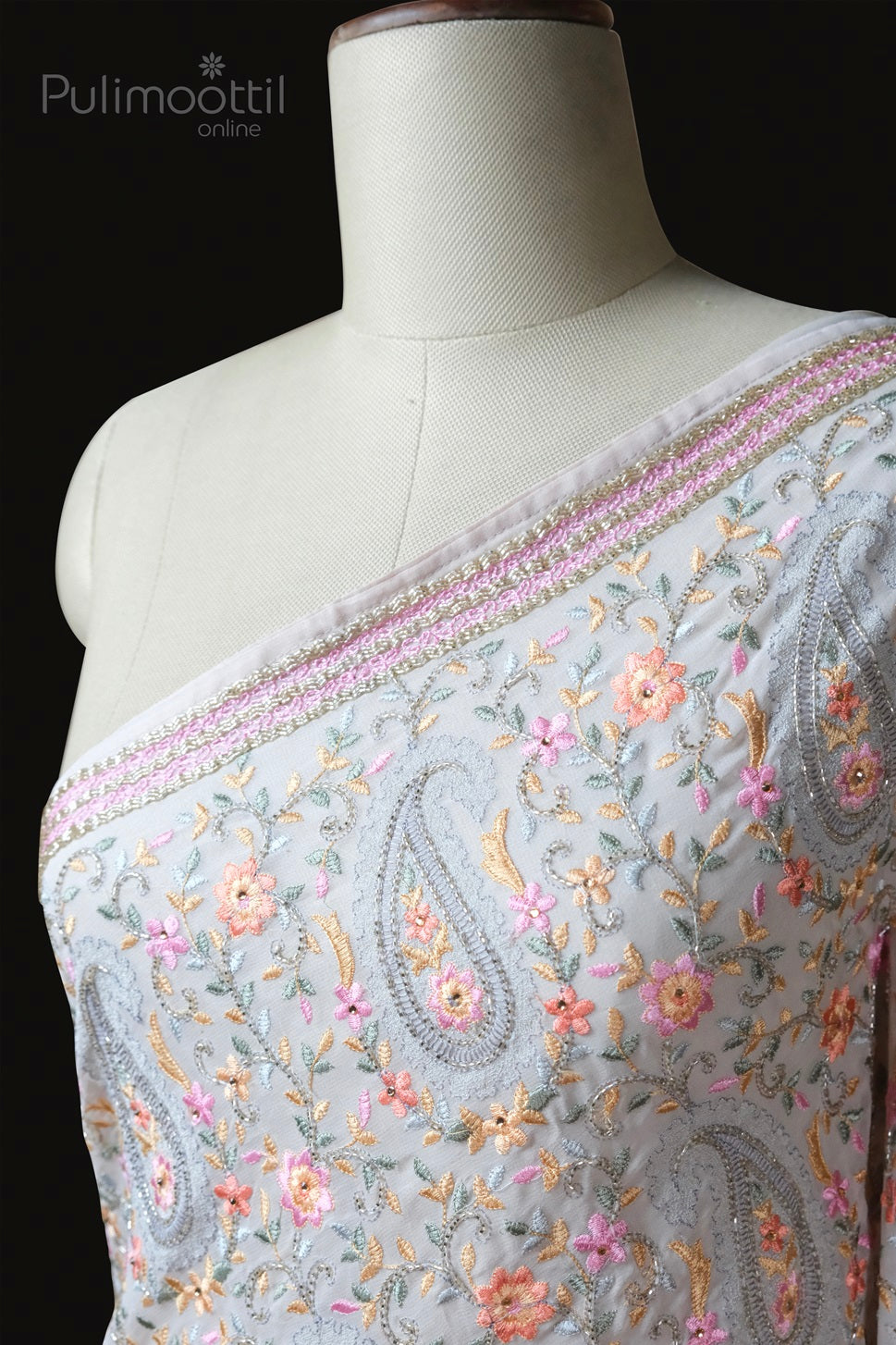 Detailed close-up of light grey net saree with pastel floral embroidery and paisley motifs, featuring a pink and gold embellished border