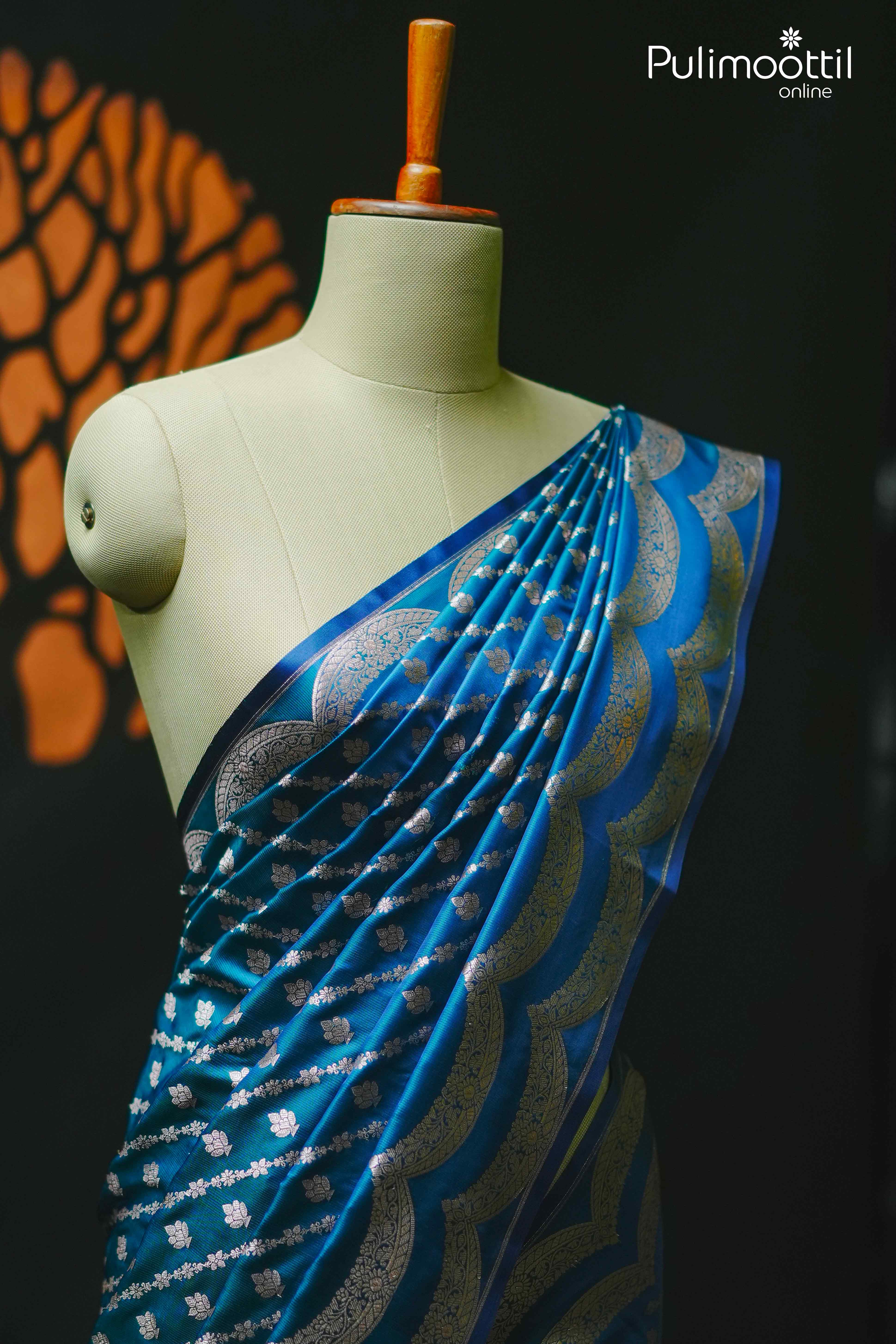 Peacock blue Banarasi silk saree with silver zari floral buttas and scallop border, draped on mannequin – Pulimoottil Online
