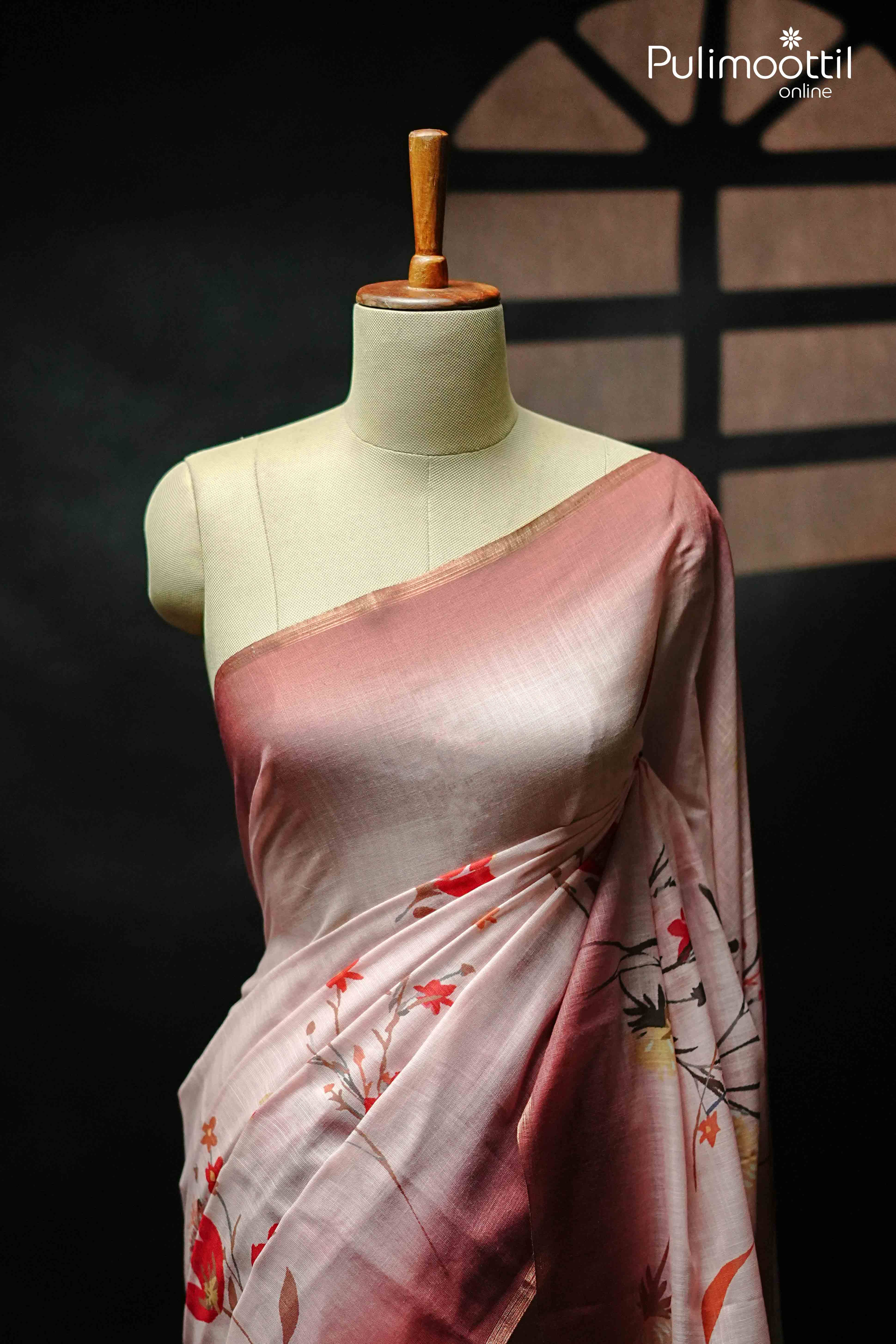 Pink semi linen saree with floral print design and subtle tissue border, draped on mannequin showcasing soft texture and graceful fall.
