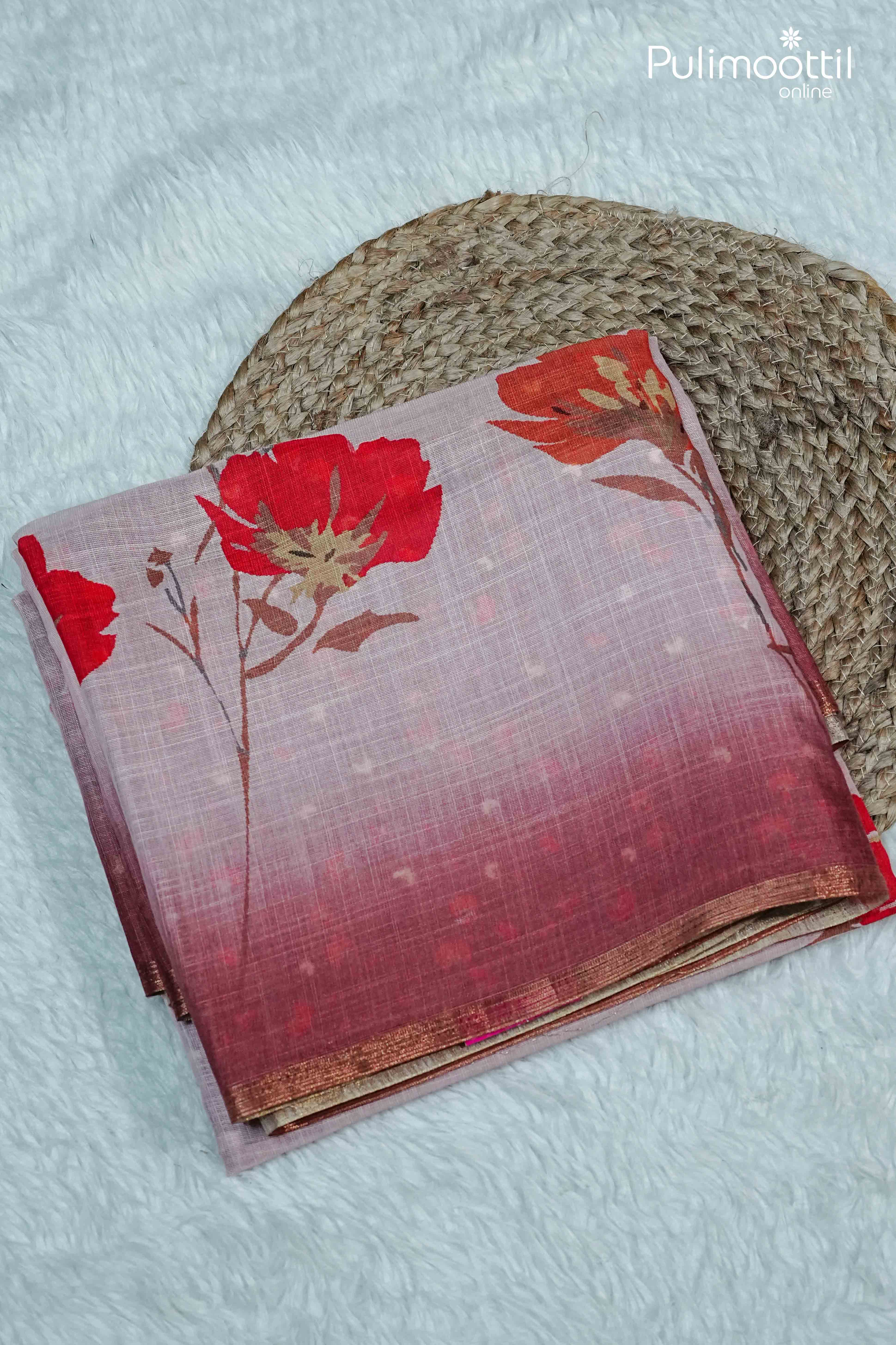 Folded pink semi linen saree with red floral print and contrast tissue border, displayed on white fur background with natural mat styling.