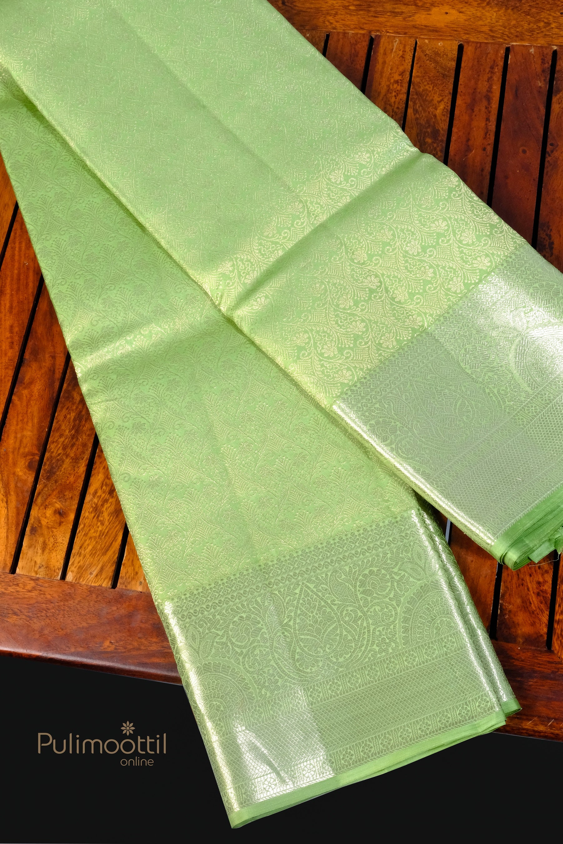 Pista green Kanchipuram silk saree with rich silver zari pallu and intricate motifs on wooden surface