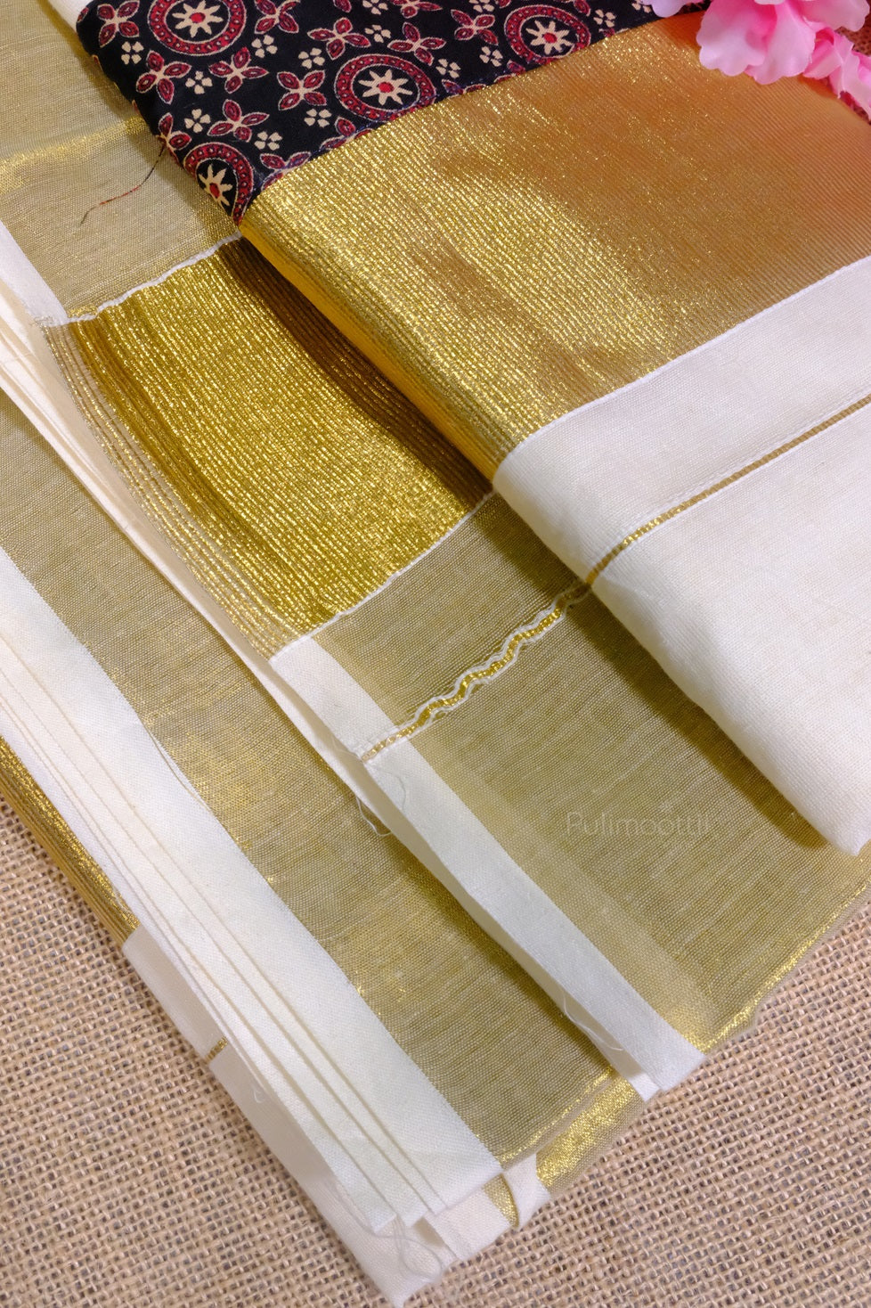 Close-up of folded pure cotton Kerala traditional Kasavu saree with golden zari border and attached black printed blouse.