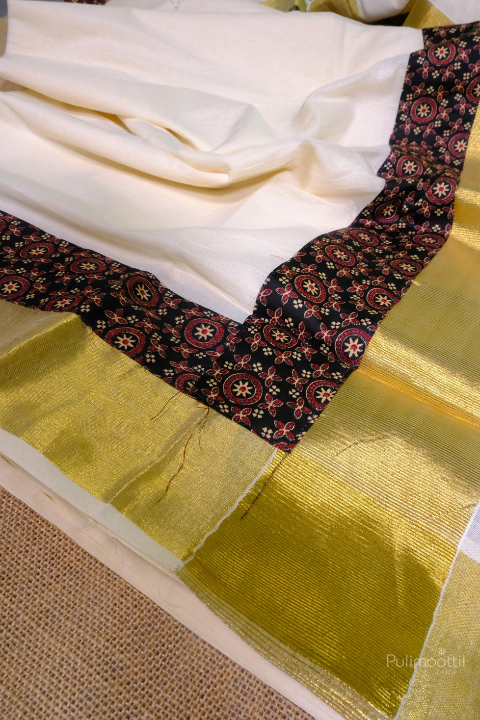 Full view of the saree spread out showing the golden border, black printed blouse, and cream cotton body.