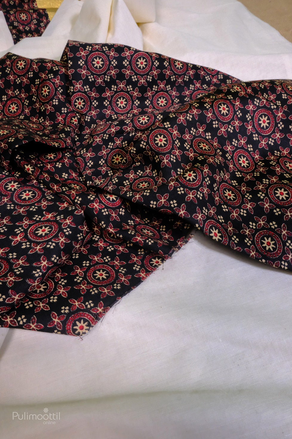 Detailed close-up of the black printed blouse fabric with floral and star motifs placed on the cream saree.
