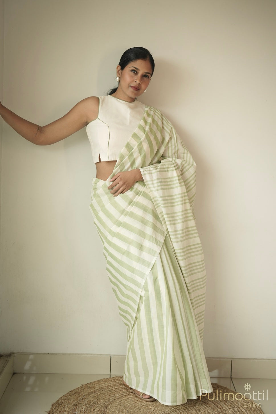 Woman wearing pastel green and cream striped handloom cotton saree with sleeveless blouse – lightweight sarees under 5000.