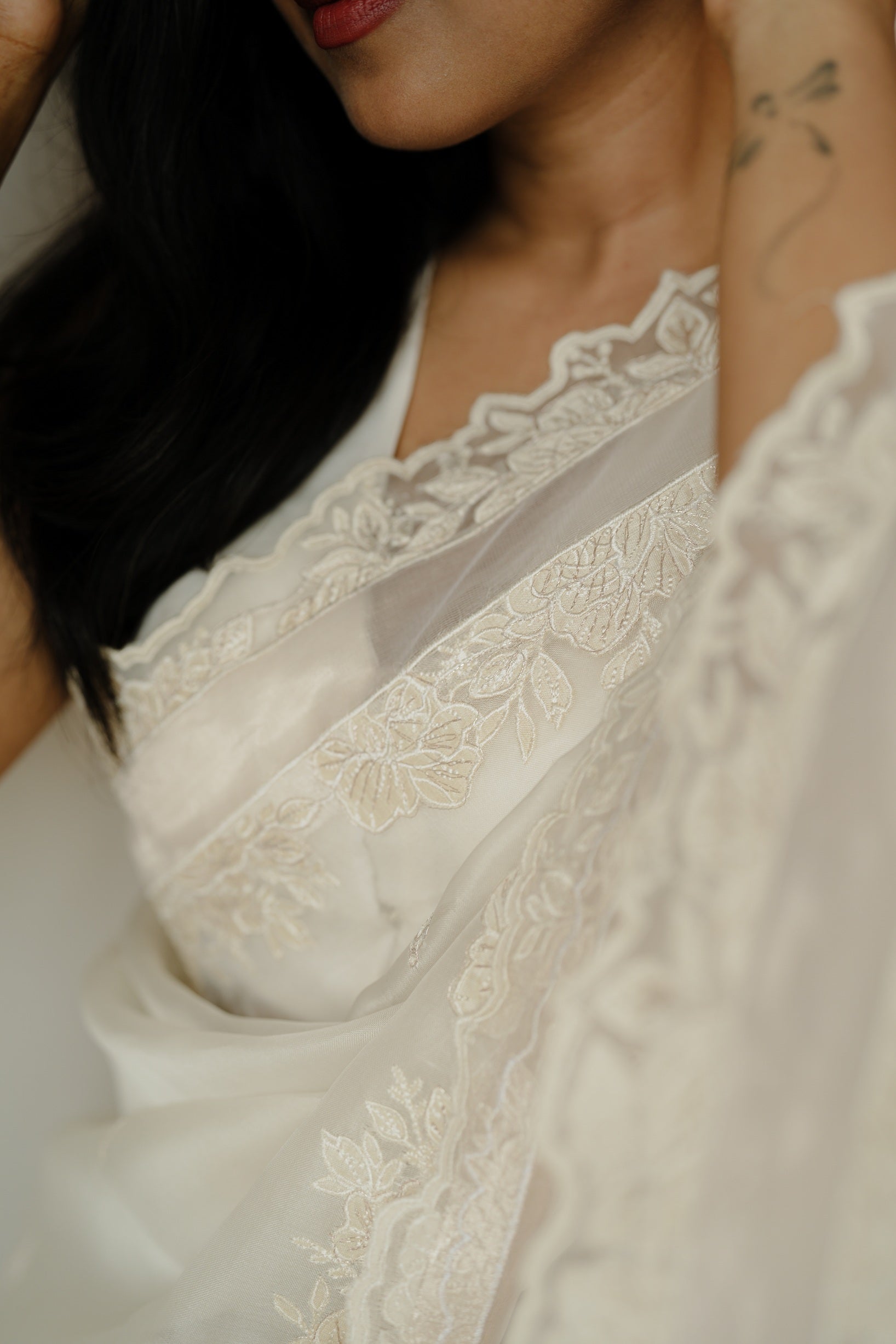 Close-up detail of an off-white saree showing intricate floral embroidery and scalloped border, highlighting the fine craftsmanship.