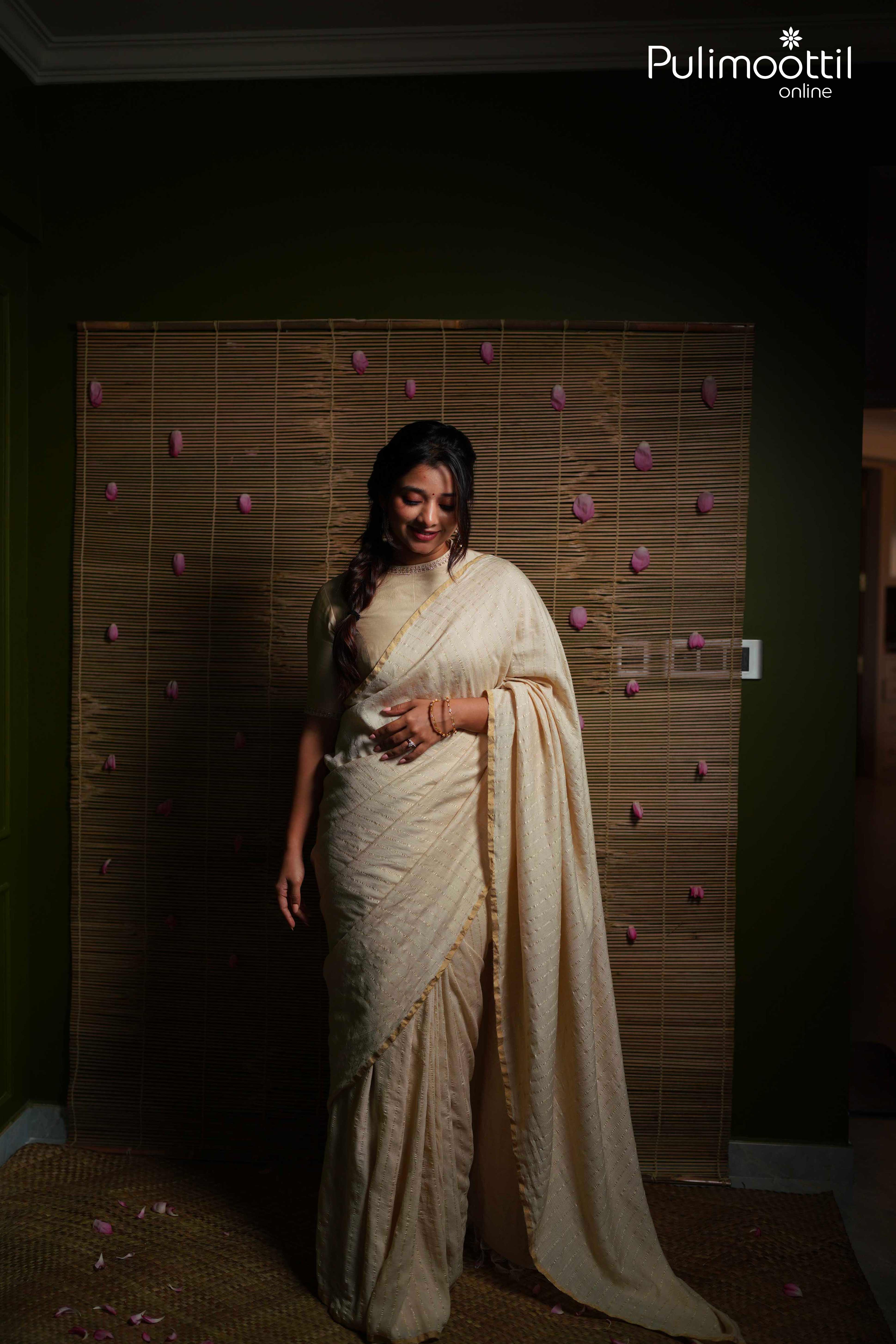 Woman draped in cream pure silk tissue saree with silver zari stripes and thin gold border, showcasing elegant traditional Kerala saree style.