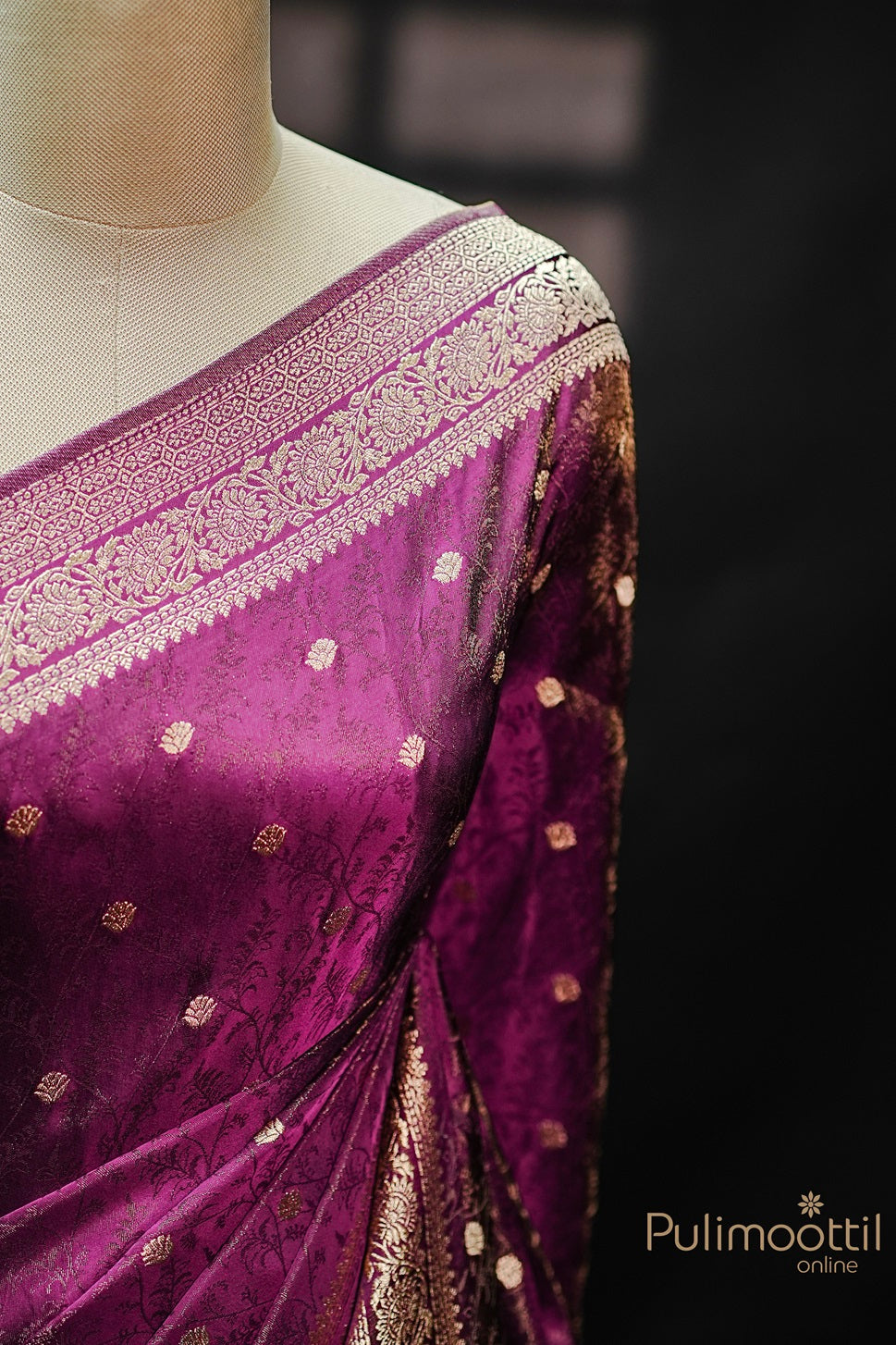 Close-up of Banarasi border on purple Uppada silk saree, featuring intricate copper zari floral weaving and small golden buttas on rich silk fabric.