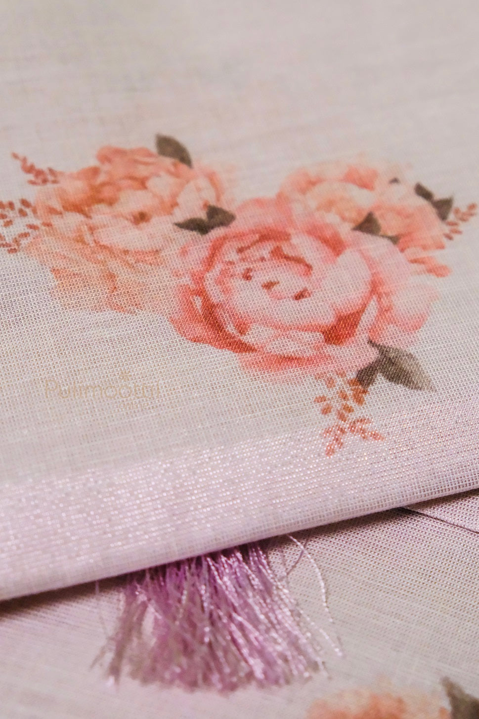 Close-up of light pink tissue Kerala saree fabric with soft pink floral print and fine texture, highlighting the intricate weave.