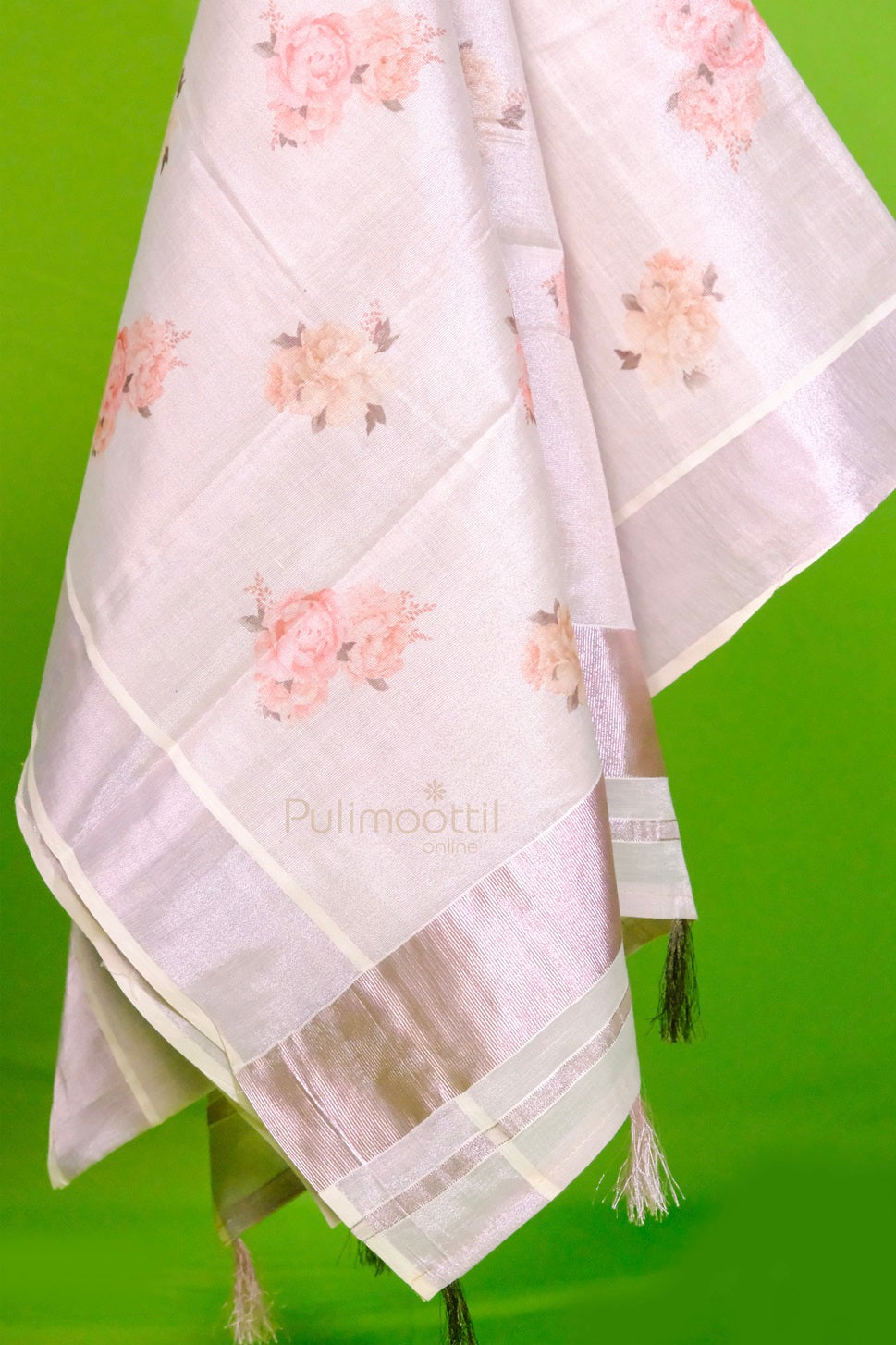 Light pink tissue Kerala saree with floral print and shimmering silver zari border, displayed against a green background.