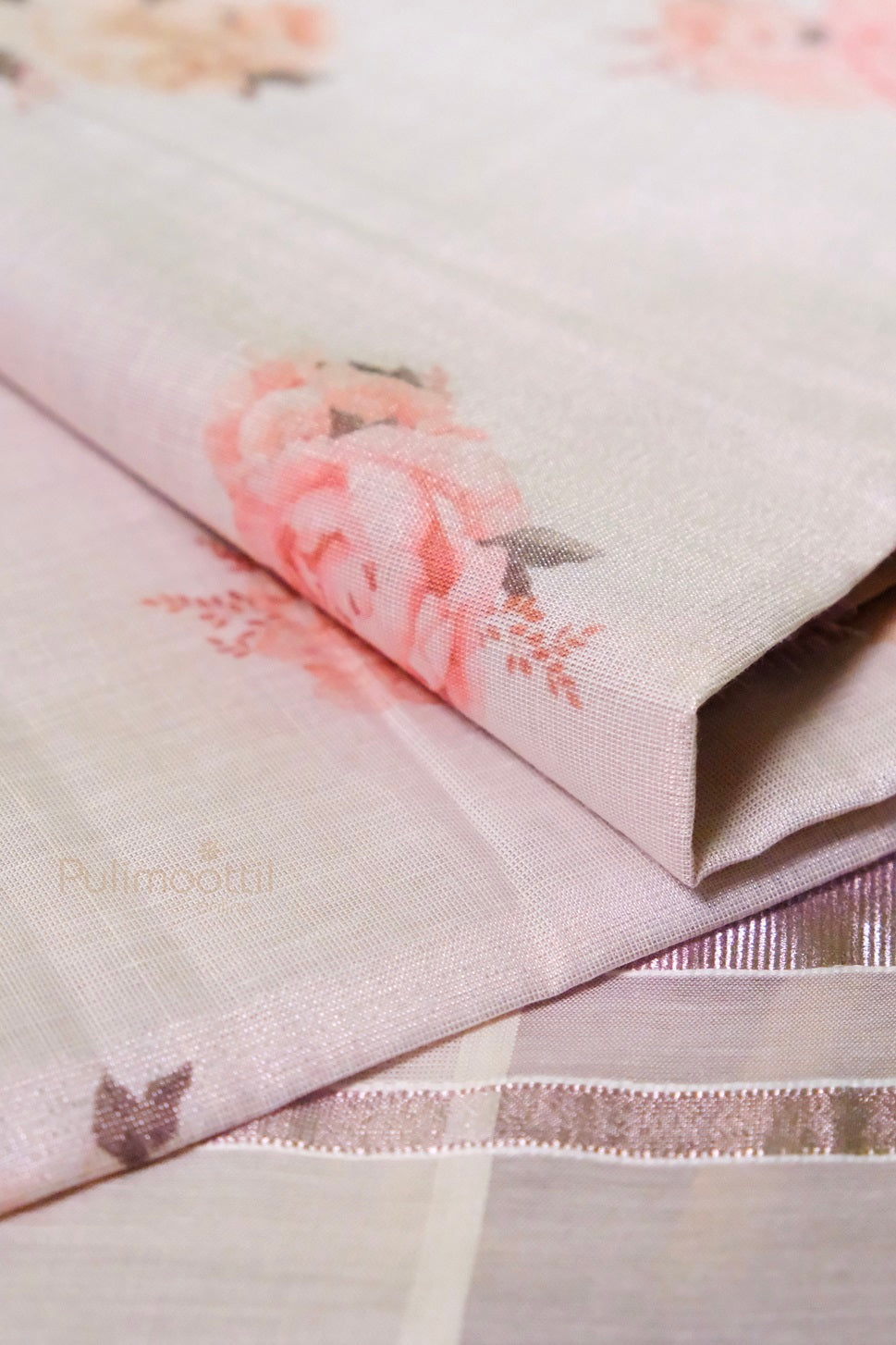 Close-up of light pink tissue Kerala saree fabric with soft pink floral print and fine texture, highlighting the intricate weave.