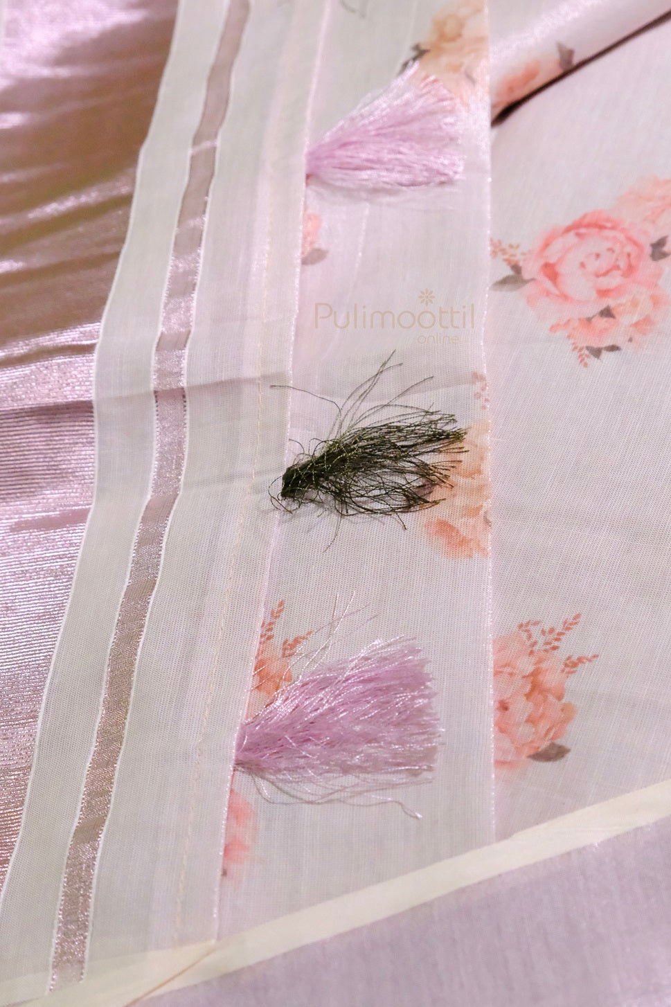 Close-up of light pink tissue Kerala saree fabric with soft pink floral print and fine texture, highlighting the intricate weave.