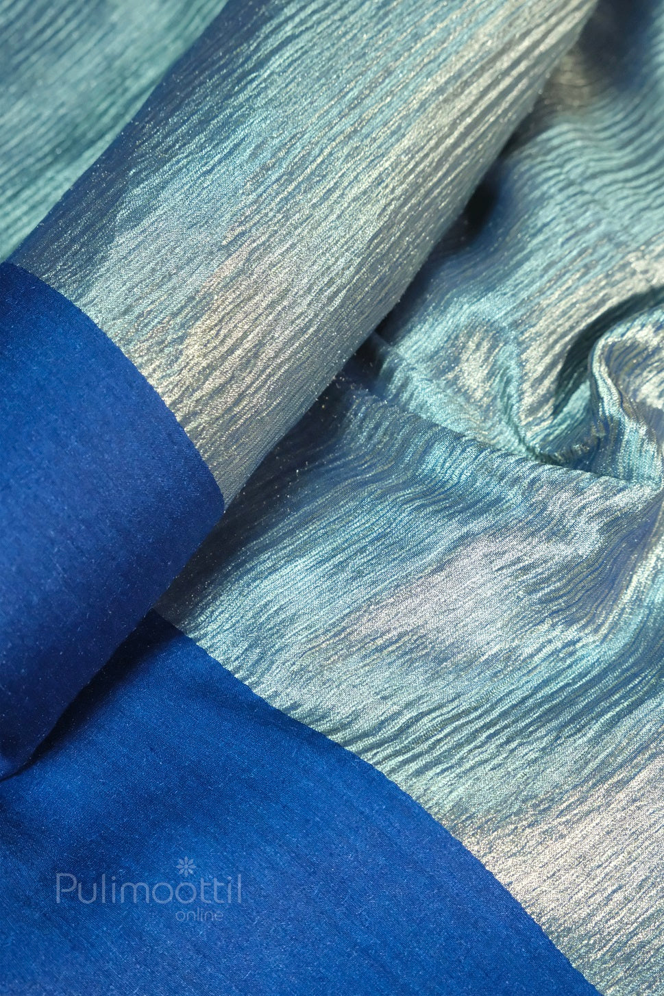 Shimmering crinkled light blue silk fabric with glossy texture and solid royal blue border, Pulimoottil Online branded textile.