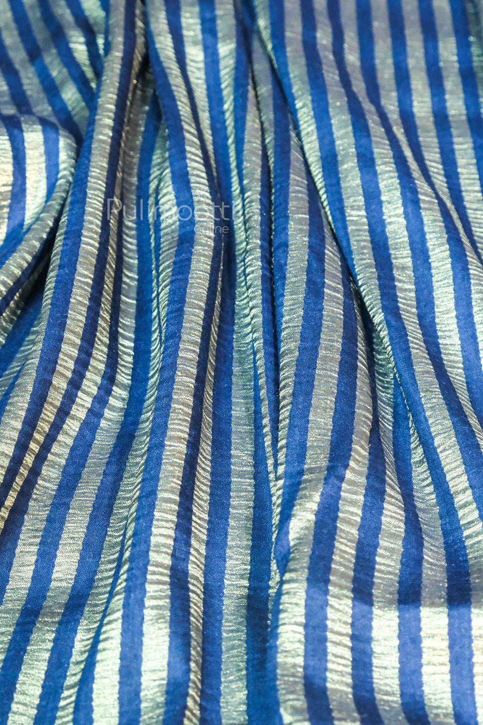 Crinkled blue and silver striped silk fabric draped with visible folds, branded Pulimoottil Online.