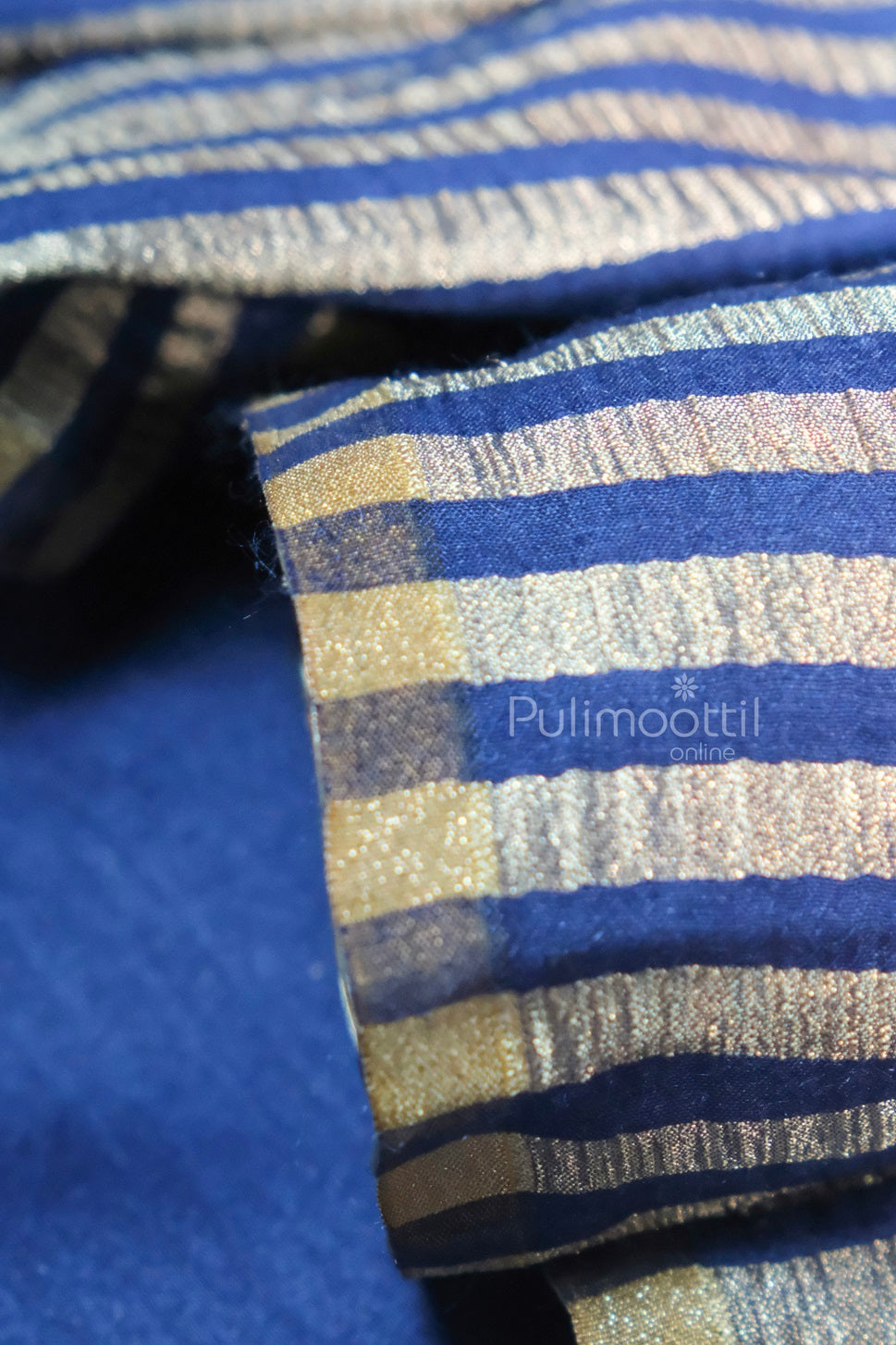Close-up of crinkled blue and gold-striped silk fabric with visible folds, branded Pulimoottil Online.