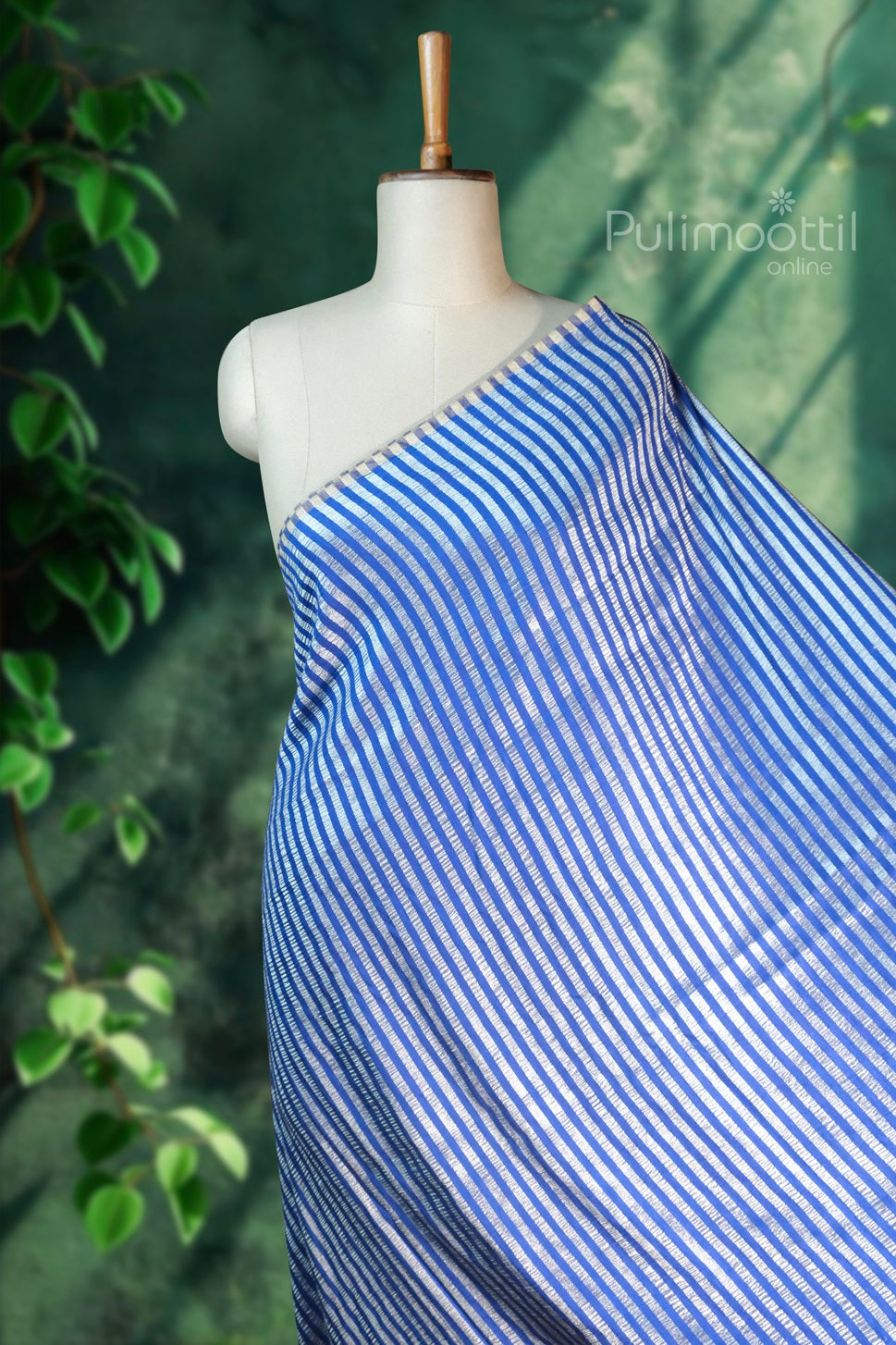 Blue and white striped saree draped on a dress form against a green background with foliage and Pulimoottil Online logo