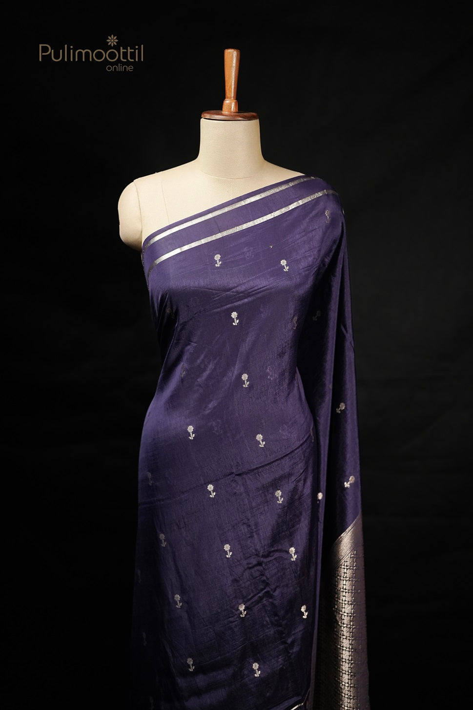 Dark violet Chiniya silk saree displayed on mannequin with light golden floral buttas and floral border, perfect as a wedding saree or party wear from Thrissur Pulimoottil Silks.