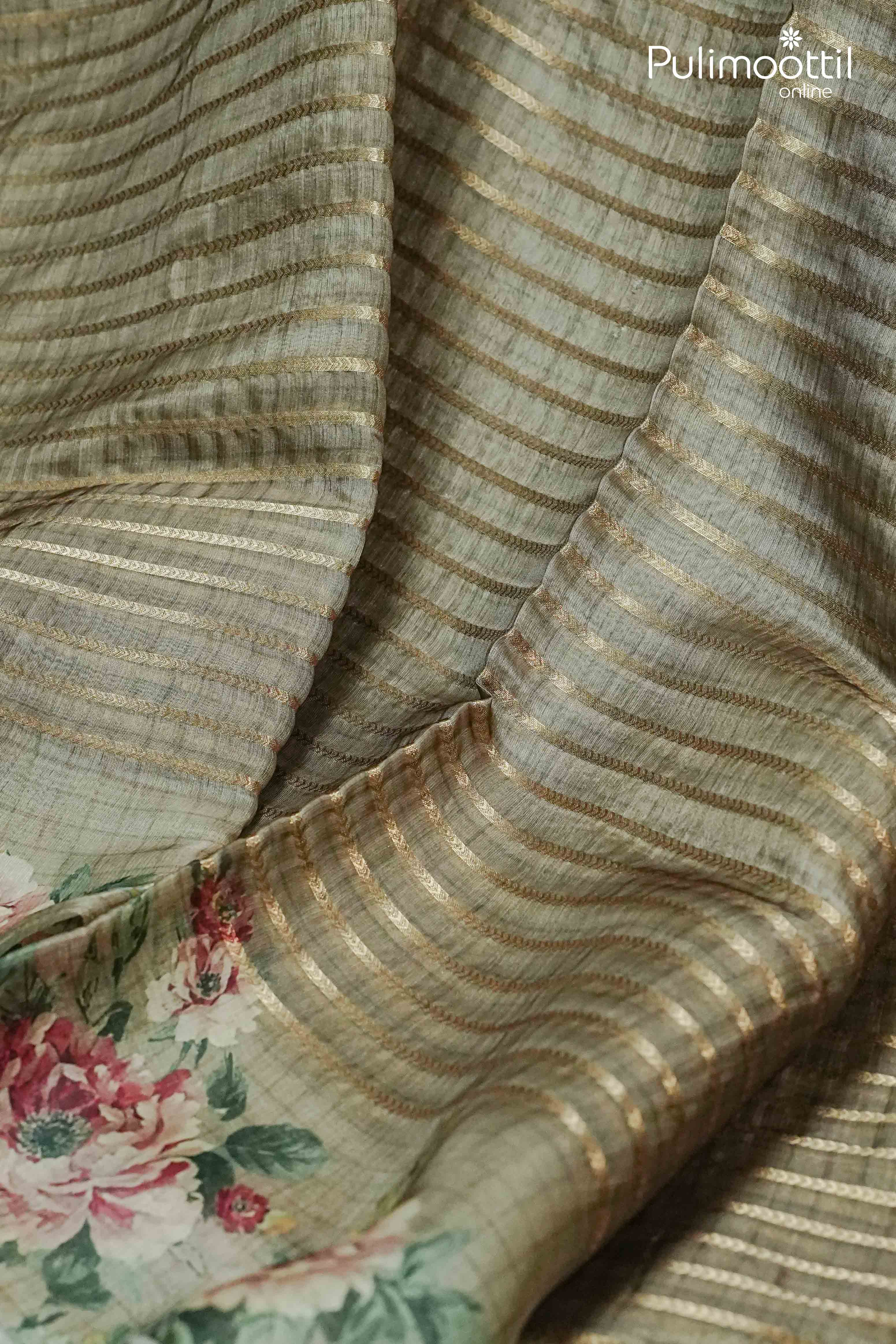 Close-up of Secret Meadow Behr green organza saree fabric featuring golden zari stripes and soft floral print—ideal for festive occasions like Onam.