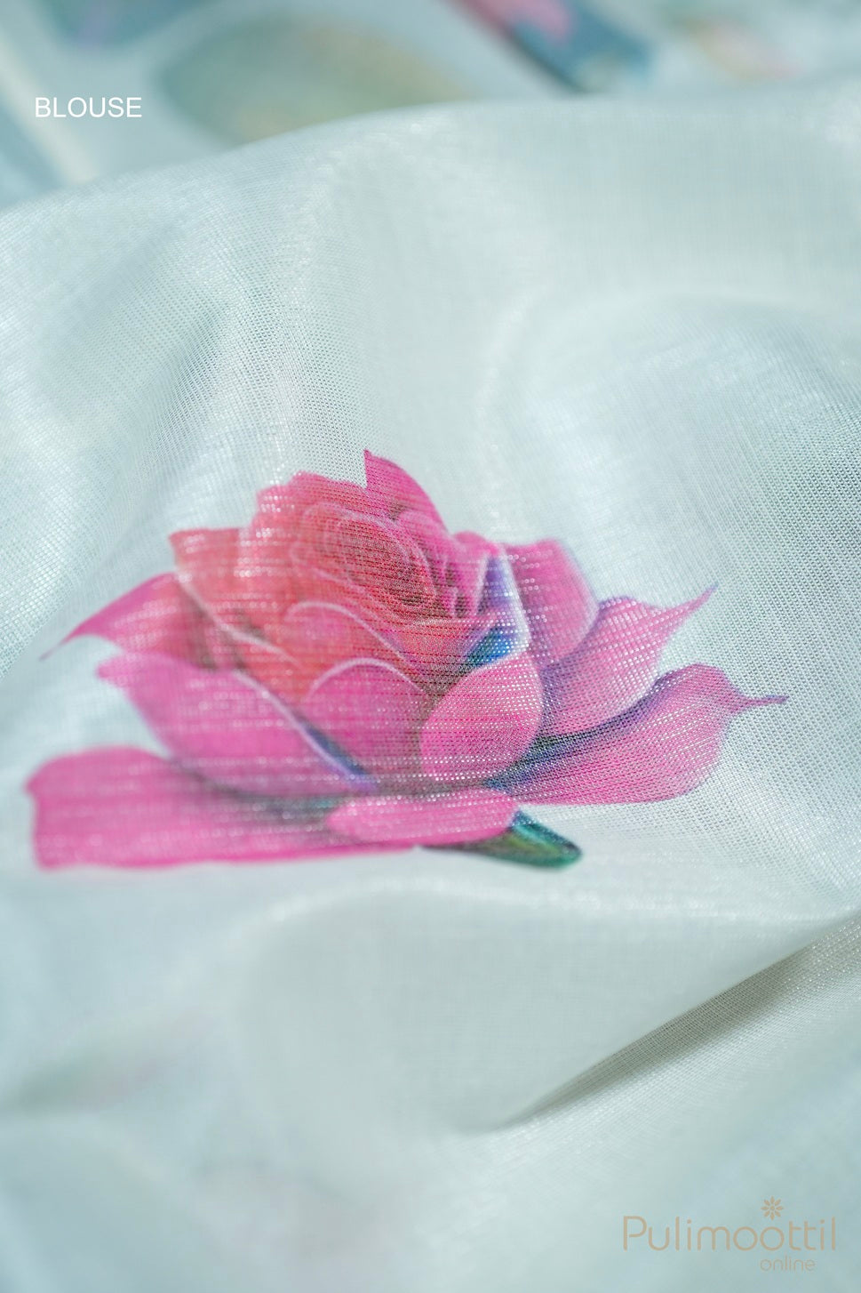 Folded silver tissue Kerala set saree with matching blouse piece showing multicolour rose floral design, placed on carpet mat over white fur cloth