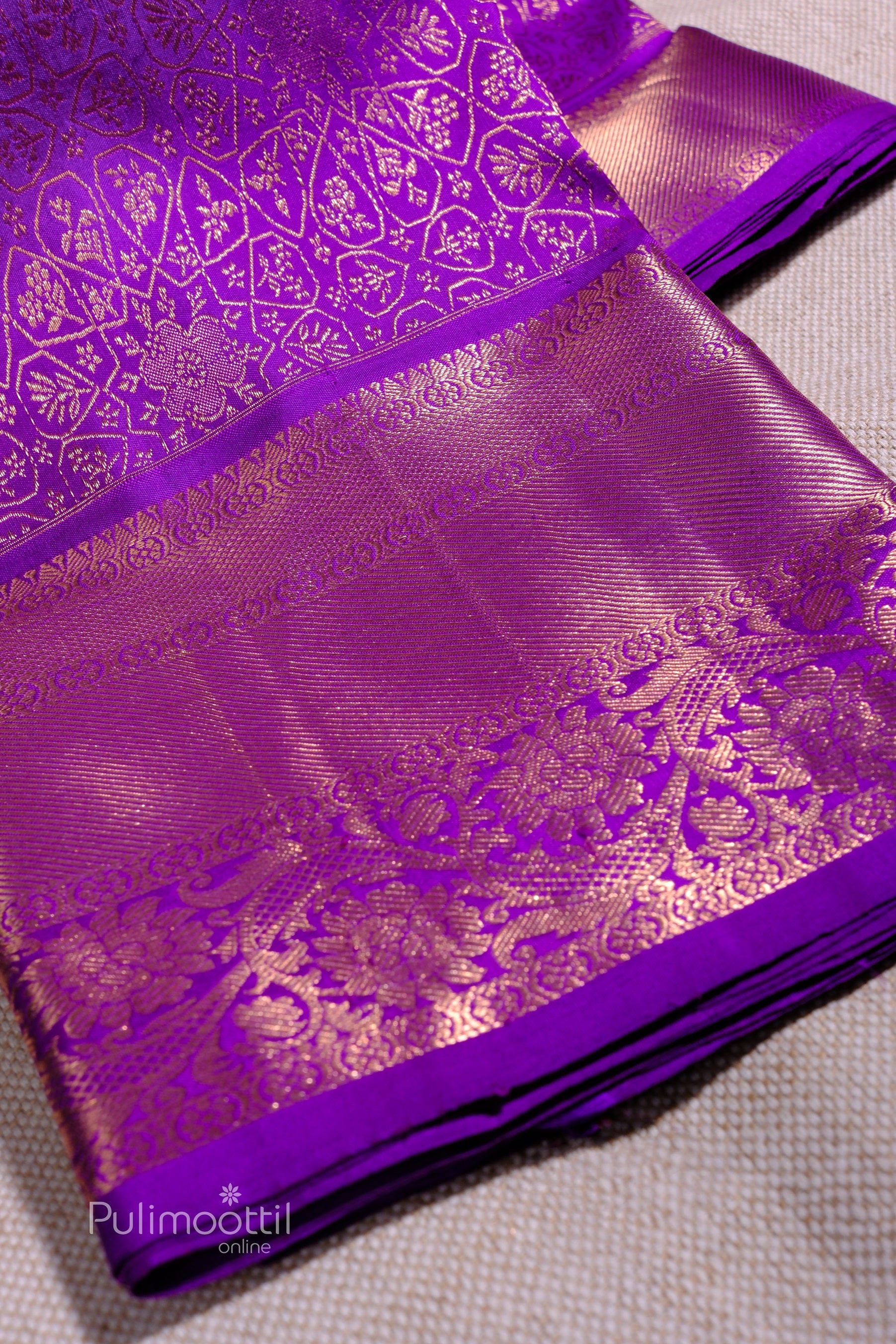 Folded violet Kanchipuram saree showcasing golden floral zari work on the border.