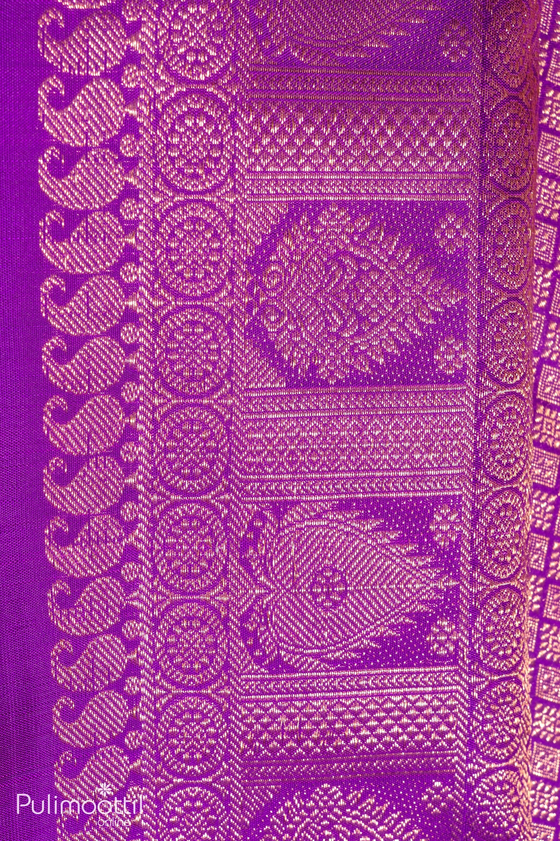 Zoomed-in view of the border design of a violet Kanchipuram saree, featuring ornate golden peacock and floral motifs.